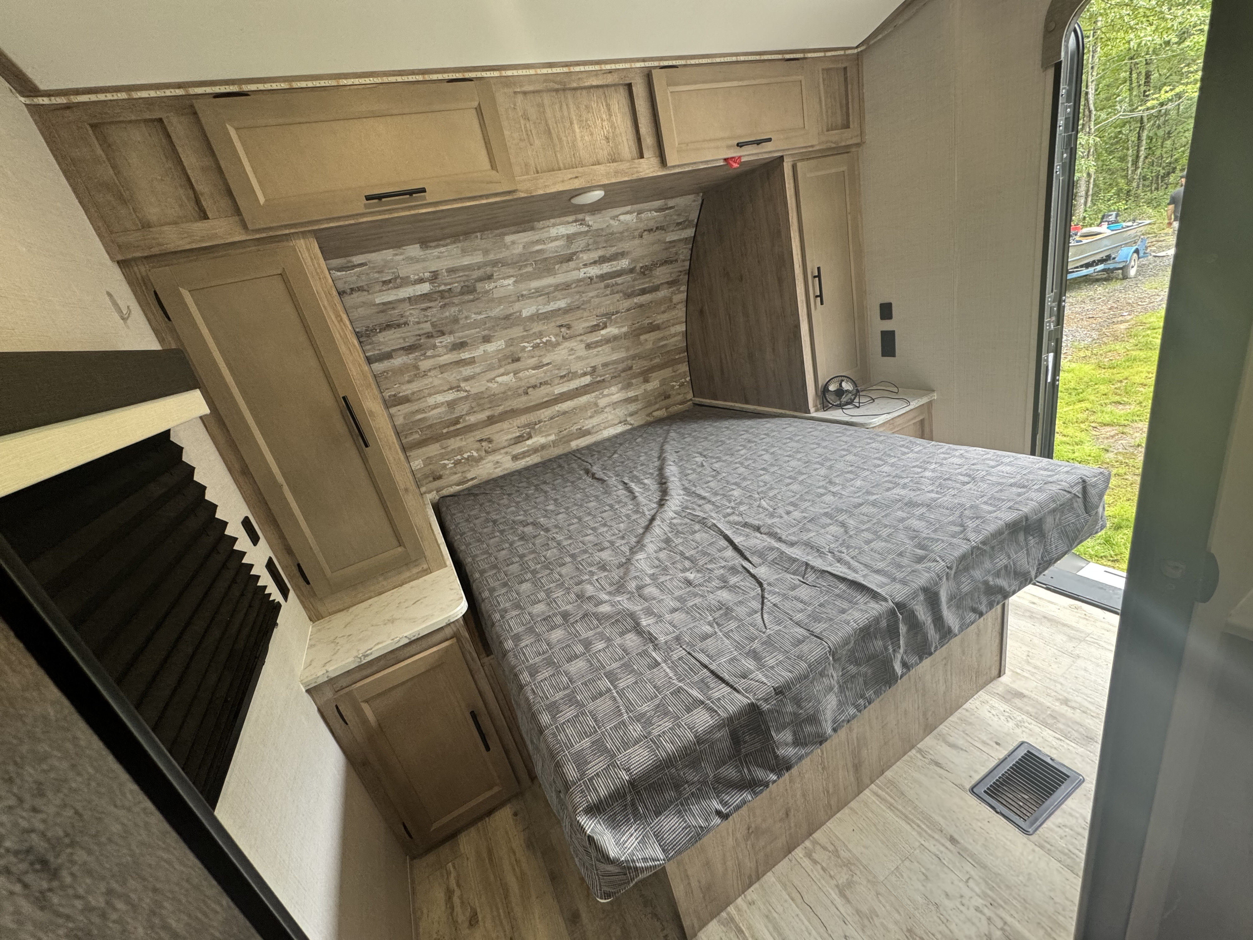 RV rental bedroom featuring a patterned bed, overhead cabinets, and a view of trees and a boat outside.. Gulf Stream Conquest Supreme 2023