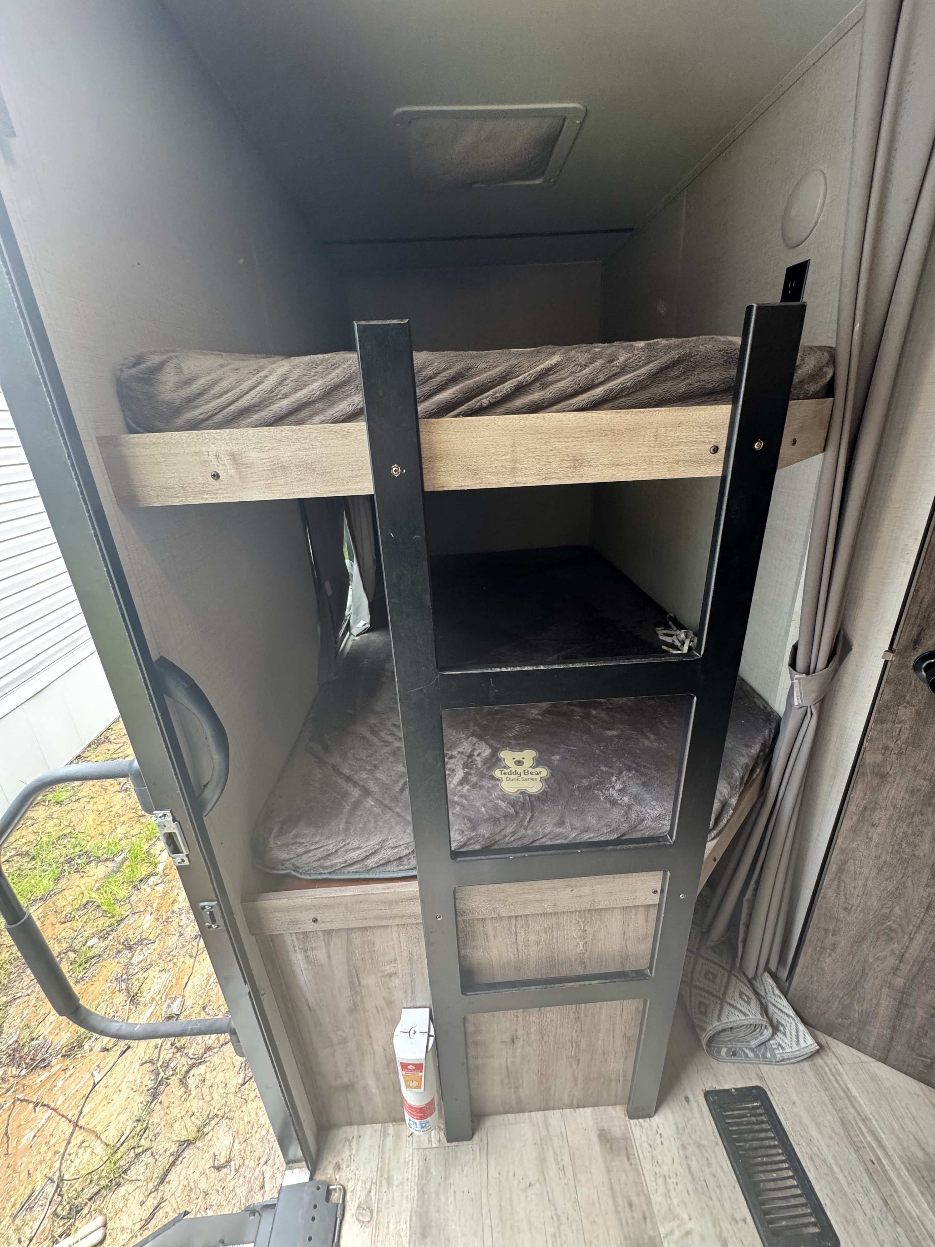 Bunk beds inside an RV rental, with dark grey bedding, a black ladder, and an emergency extinguisher. Ideal for family trips.. Gulf Stream Conquest Supreme 2023