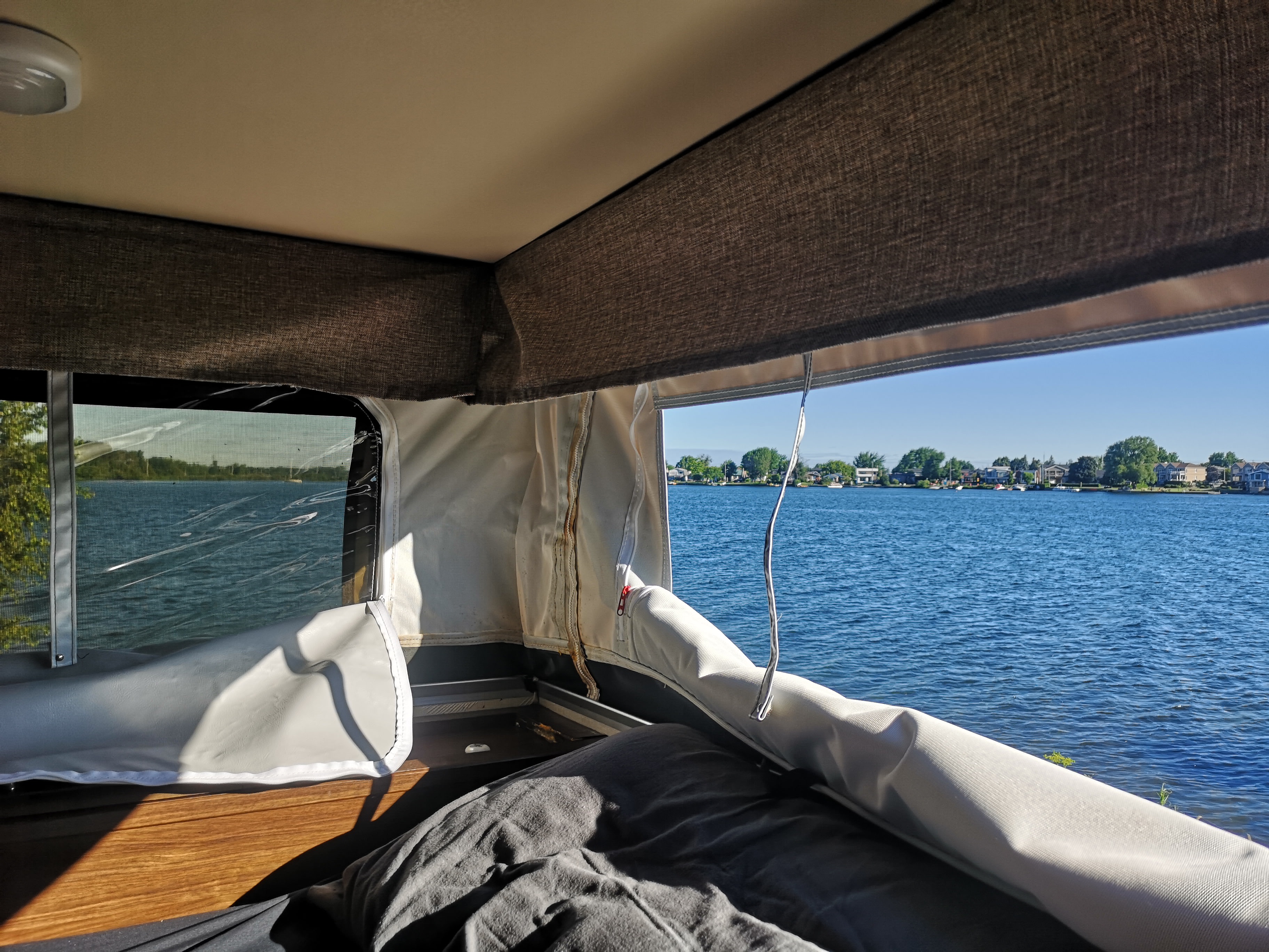 An interior view of a pop-up RV rental showing a bed & lake view with houses on the far shore. Perfect for nature escapes.. Palomino Backpack Edition 2018
