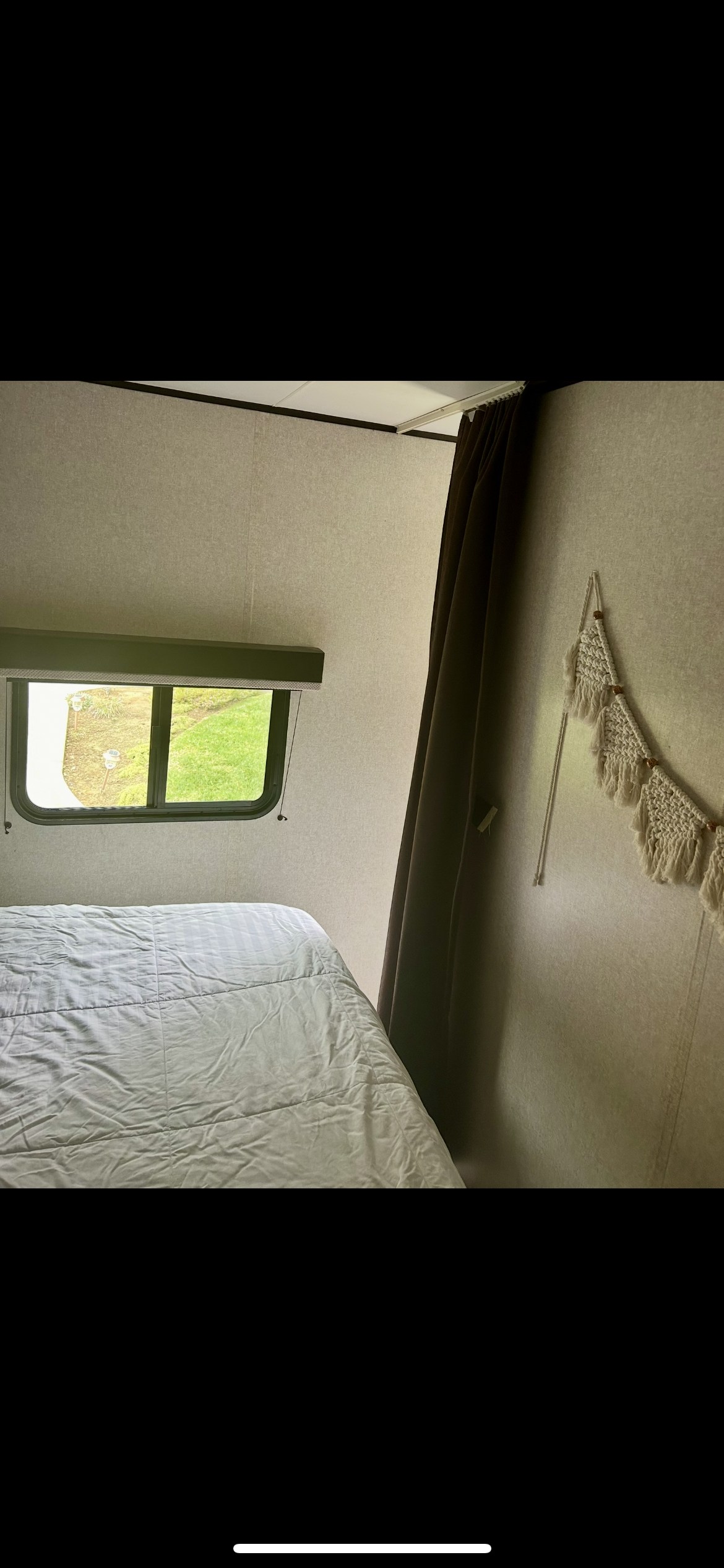 RV rental bedroom with neat white bed, window showcasing green scenery, and boho macrame wall art.. Jayco Jay Flight SLX 2018