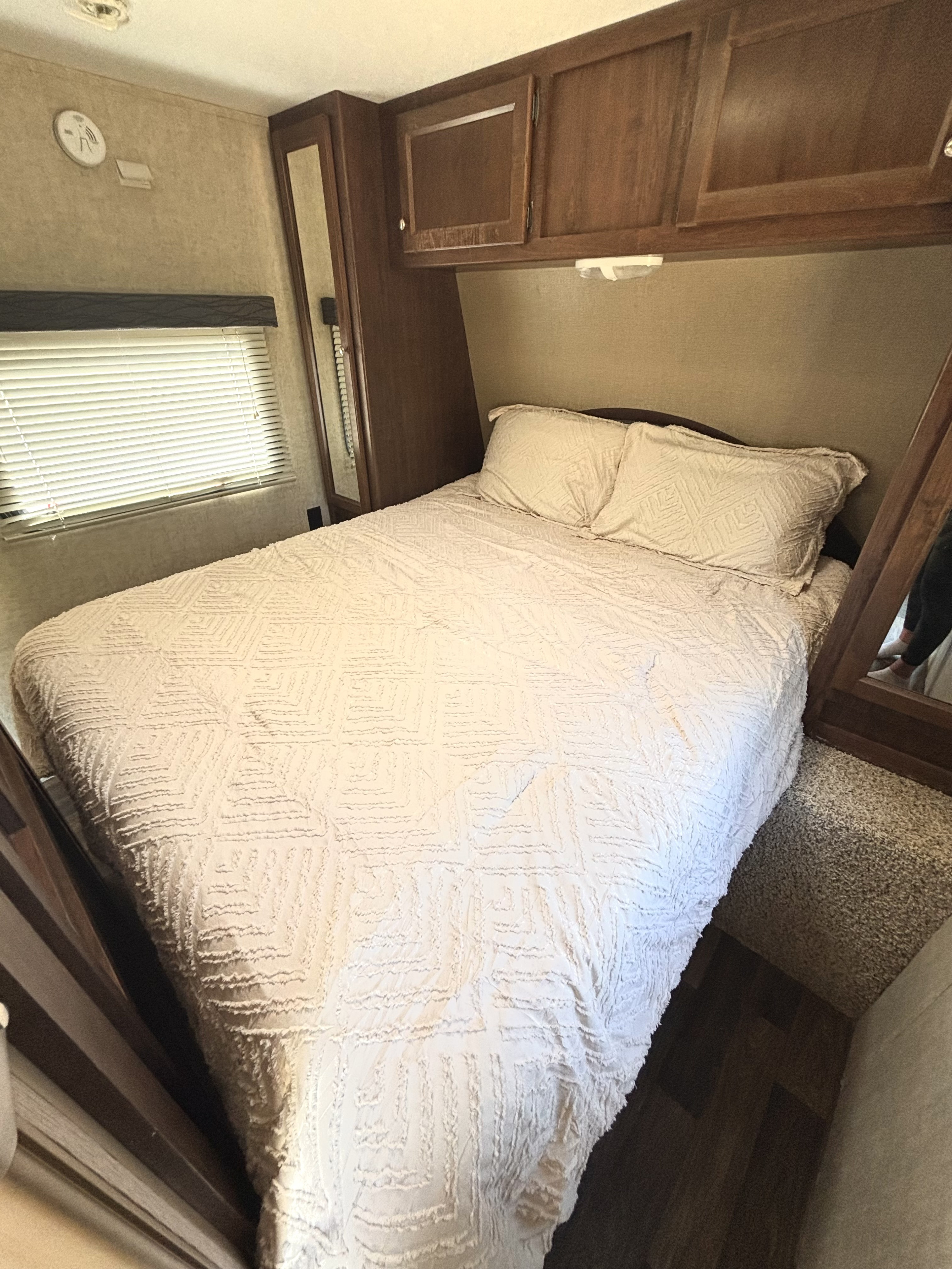 Experience comfort in this rv rental bedroom featuring a bed with textured comforter, overhead cabinets, and blinds.. Keystone Hideout 2015