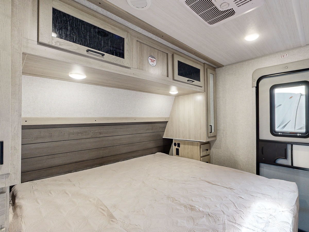 Inside a spacious RV rental bedroom, showcasing a queen bed, wood paneling, and convenient overhead cabinets.. Forest River Alta 2025