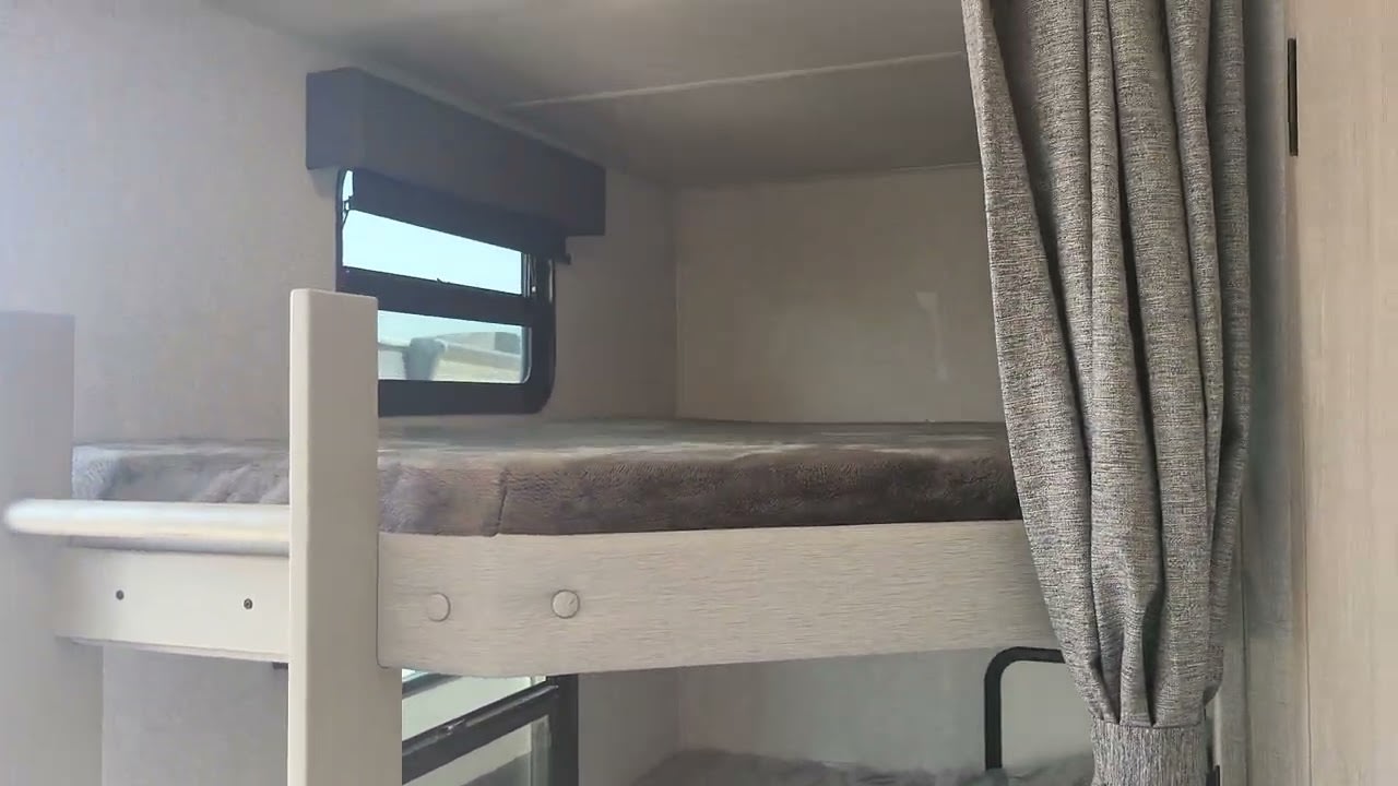 Cozy bunk beds inside an RV rental, perfect for family adventures. Features a window and privacy curtain.. Forest River Alta 2025