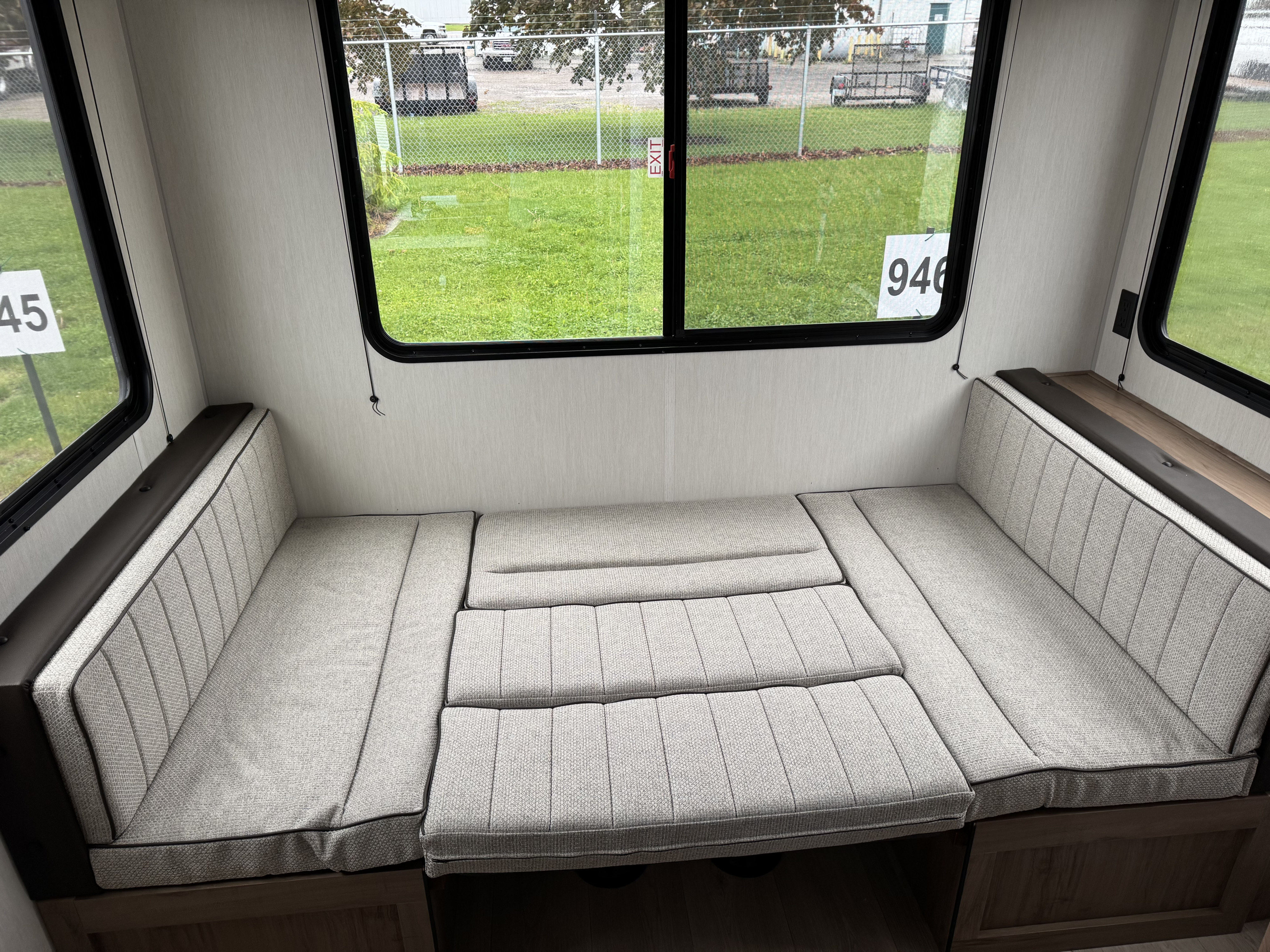 Inside an RV rental: light grey dinette cushions transform into a bed, seen through large windows revealing a fenced outdoor area.. Forest River 20RDSE 2025