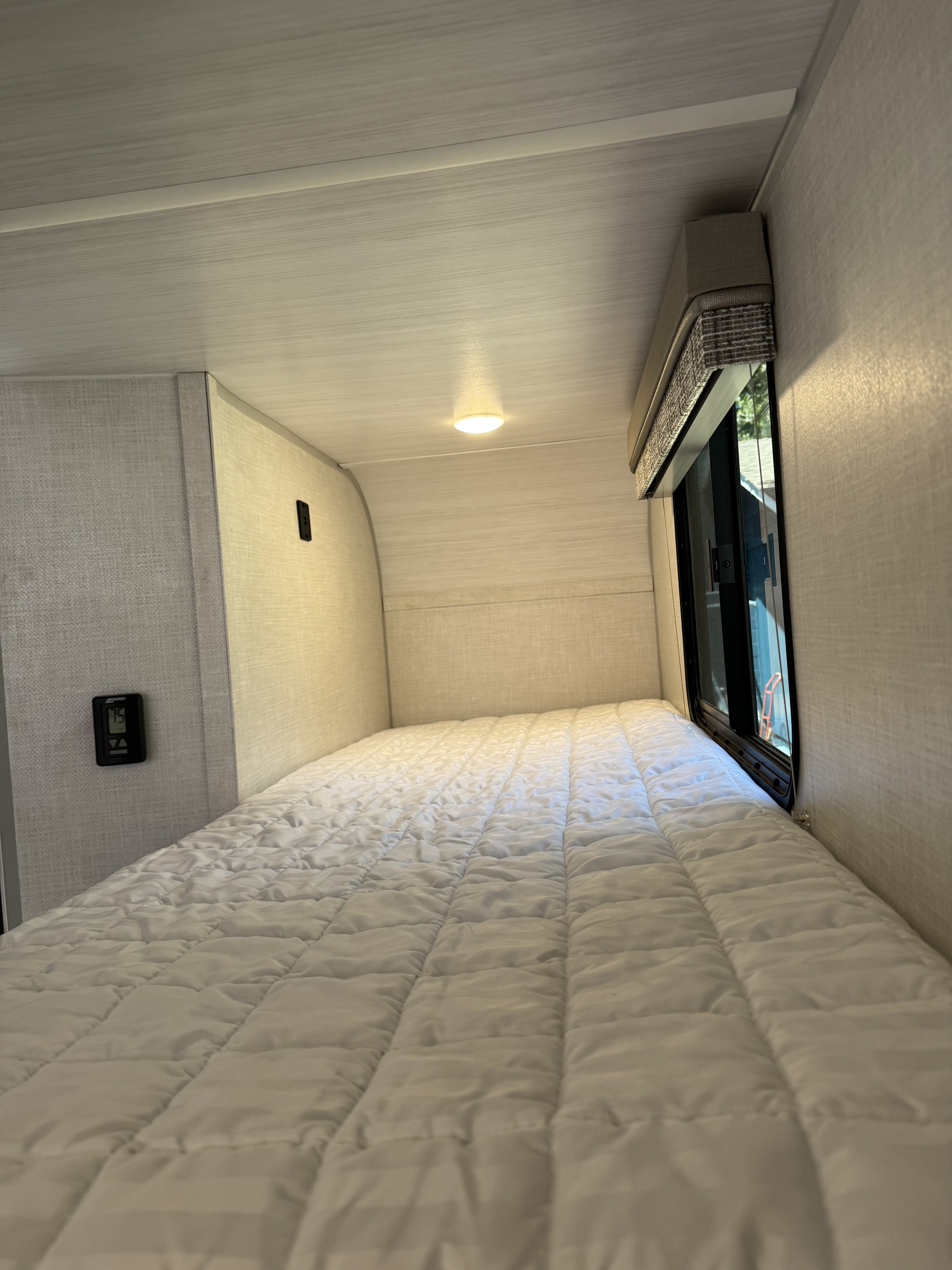 Comfortable RV rental sleeping area features a quilted bed, window with blind, ceiling light, and thermostat.. Forest River r-pod 193 2022