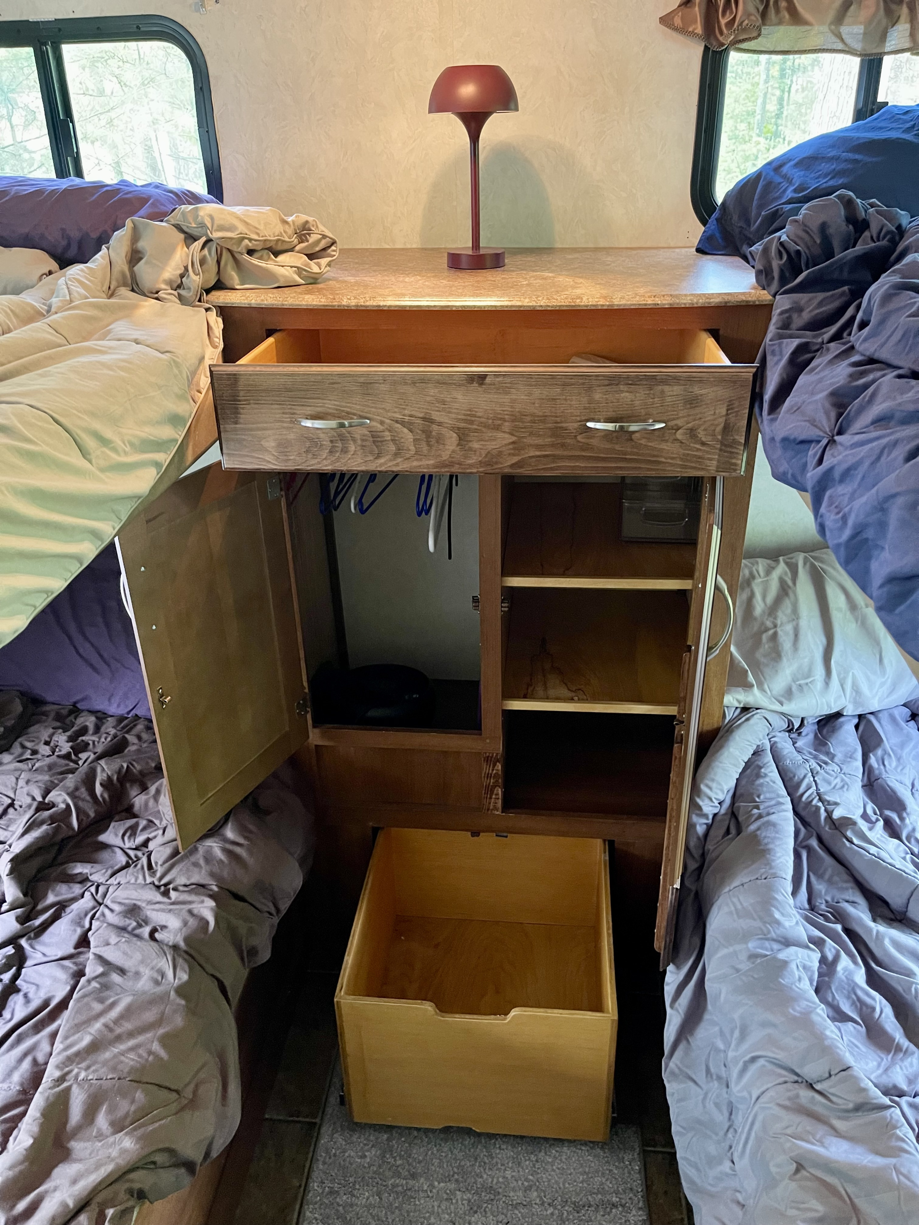 RV rental interior: bunk beds frame a versatile storage unit with open drawer, cabinet, and a lamp, ideal for travel organization.. Coachmen Freedom Express 2013