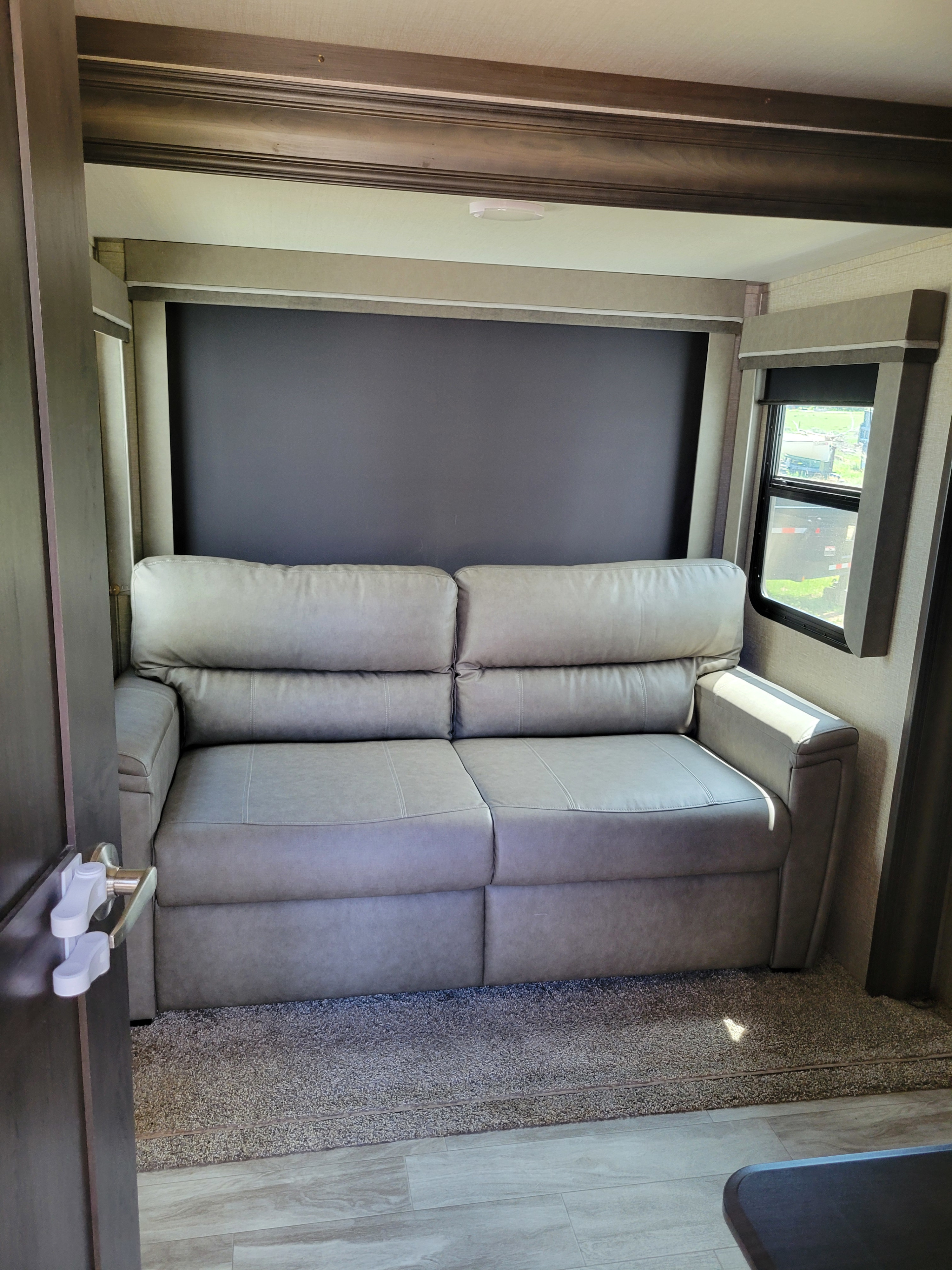 RV rental living area: A comfortable gray sofa in a modern RV interior with a window view, offering a cozy living space.. Grand Design Reflection 2020