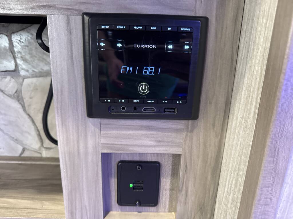 This RV rental's Furrion infotainment system displays FM 88.1, with a power button visible. A USB charging port is below, built into the wood paneling.. Forest River Cherokee Alpha Wolf 2020