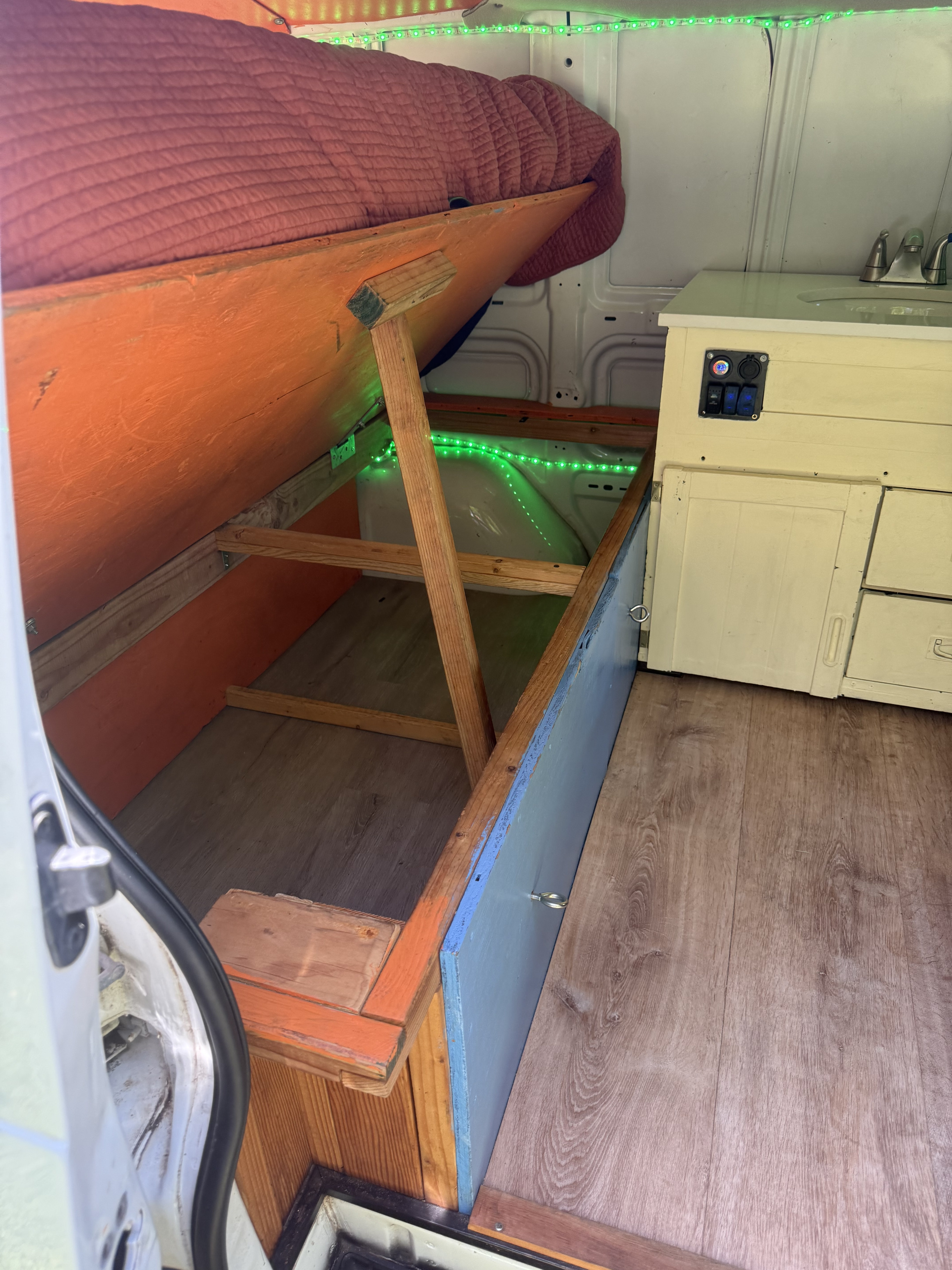 This RV rental's van interior features lifted bed storage with green LEDs, a compact kitchen, and wood-look flooring.. Chevrolet Other 2005