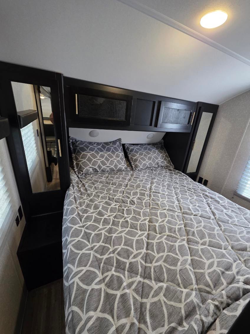 Cozy RV rental bedroom with a gray patterned bed, overhead cabinets, built-in mirrors, and storage. Functional interior.. Forest River Cherokee Grey Wolf 2022