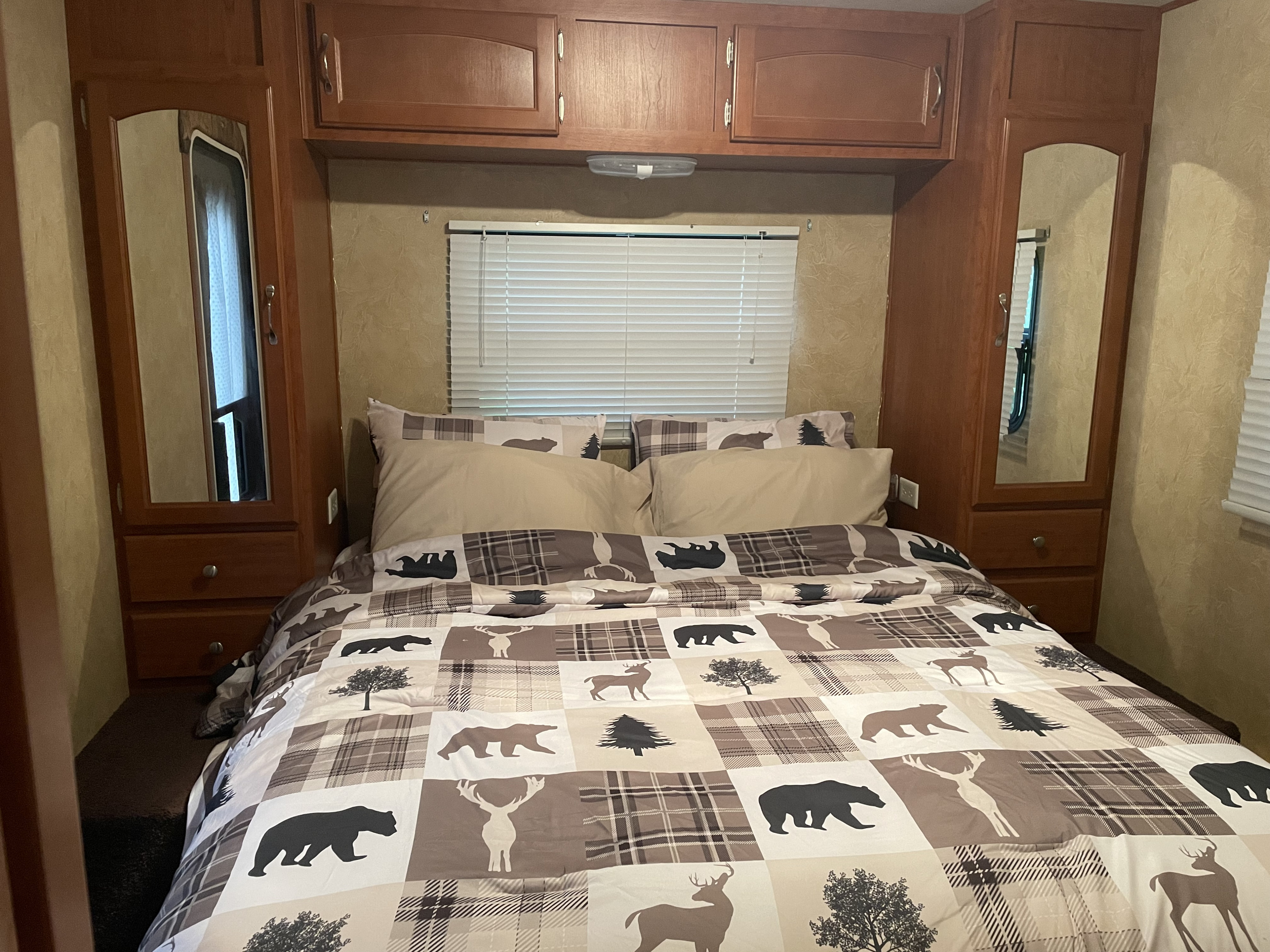 Cozy RV rental bedroom features a plaid and wildlife-themed comforter, wooden cabinets, and a window with blinds.. Forest River Wildwood LA 2009