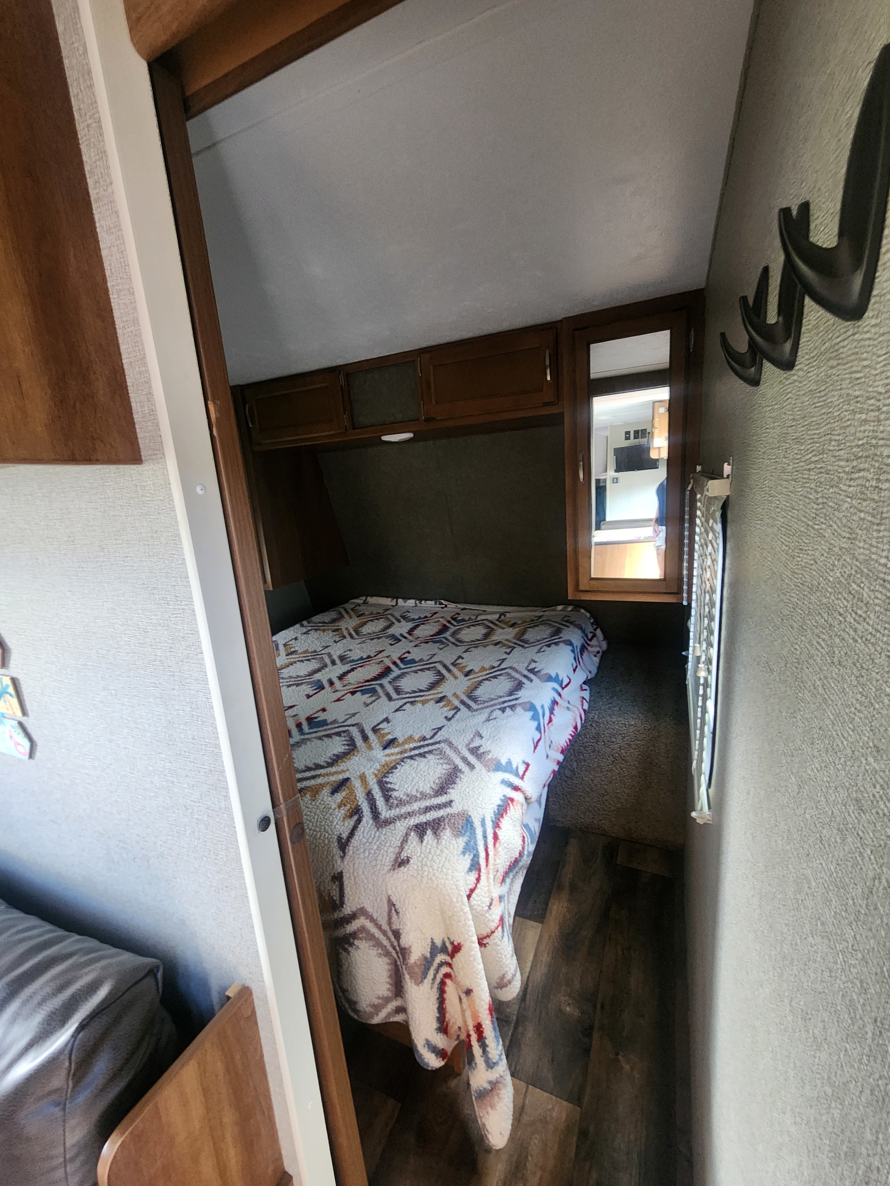 RV rental bedroom view: Features a patterned bed, overhead cabinets, and a mirror reflecting the living area.. Keystone RV Springdale 2018
