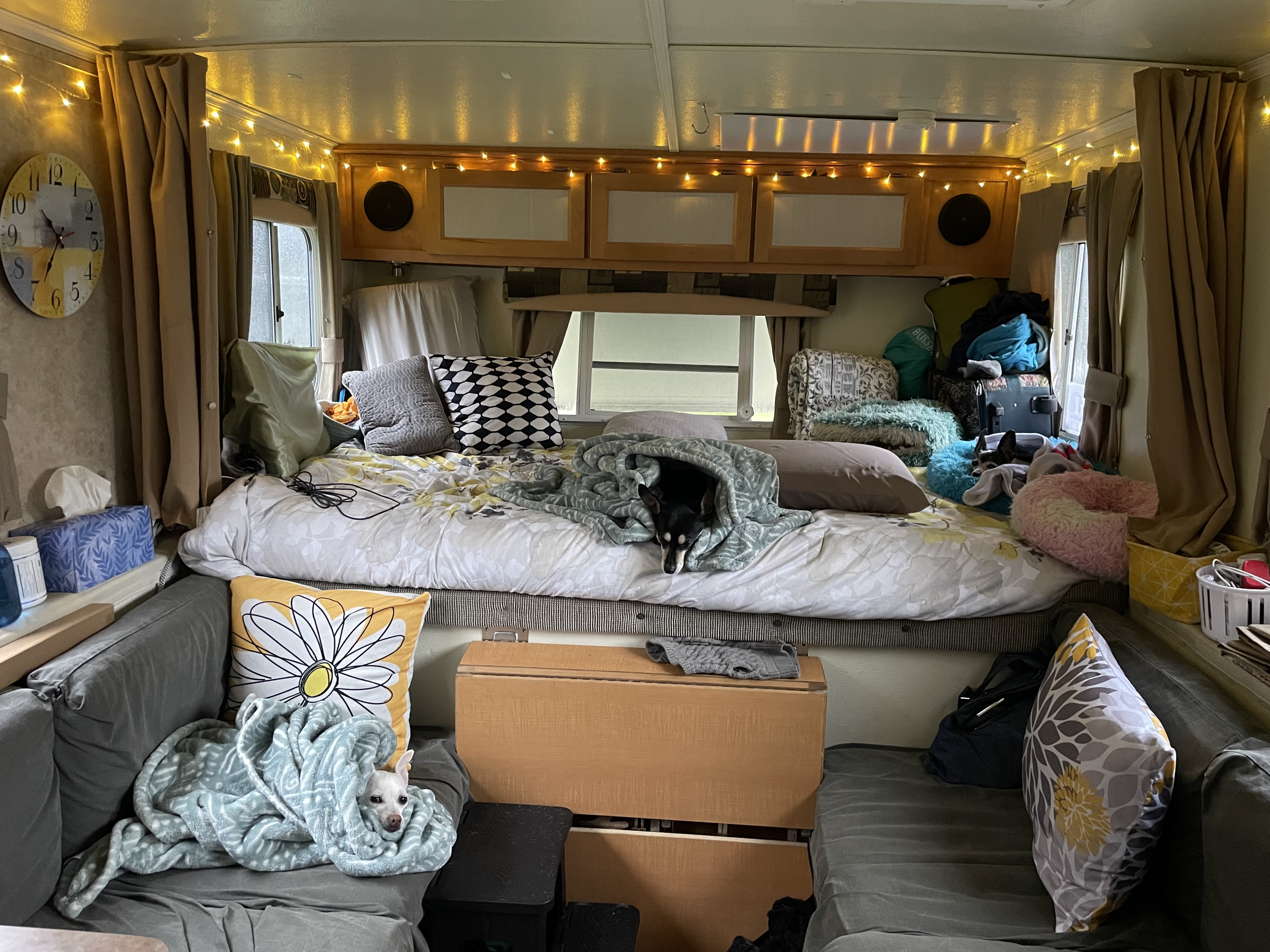 Cozy RV rental interior features a comfortable bed with a black dog, couches with a white dog snuggled in a blanket, and warm string lights.. TrailManor 2720 QB 2009