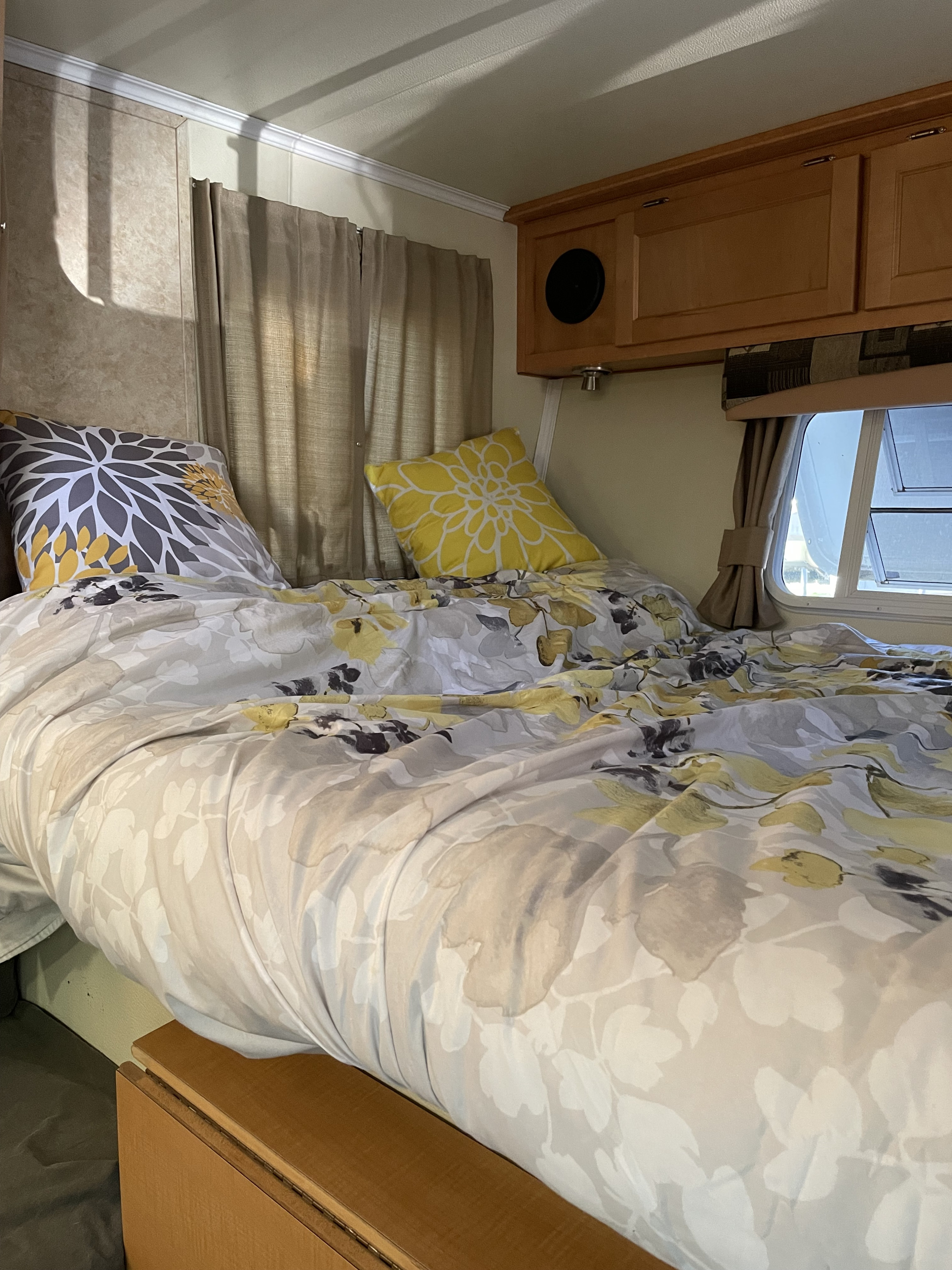Cozy RV rental bedroom with floral bedding, accent pillows, wood cabinets, and windows.. TrailManor 2720 QB 2009