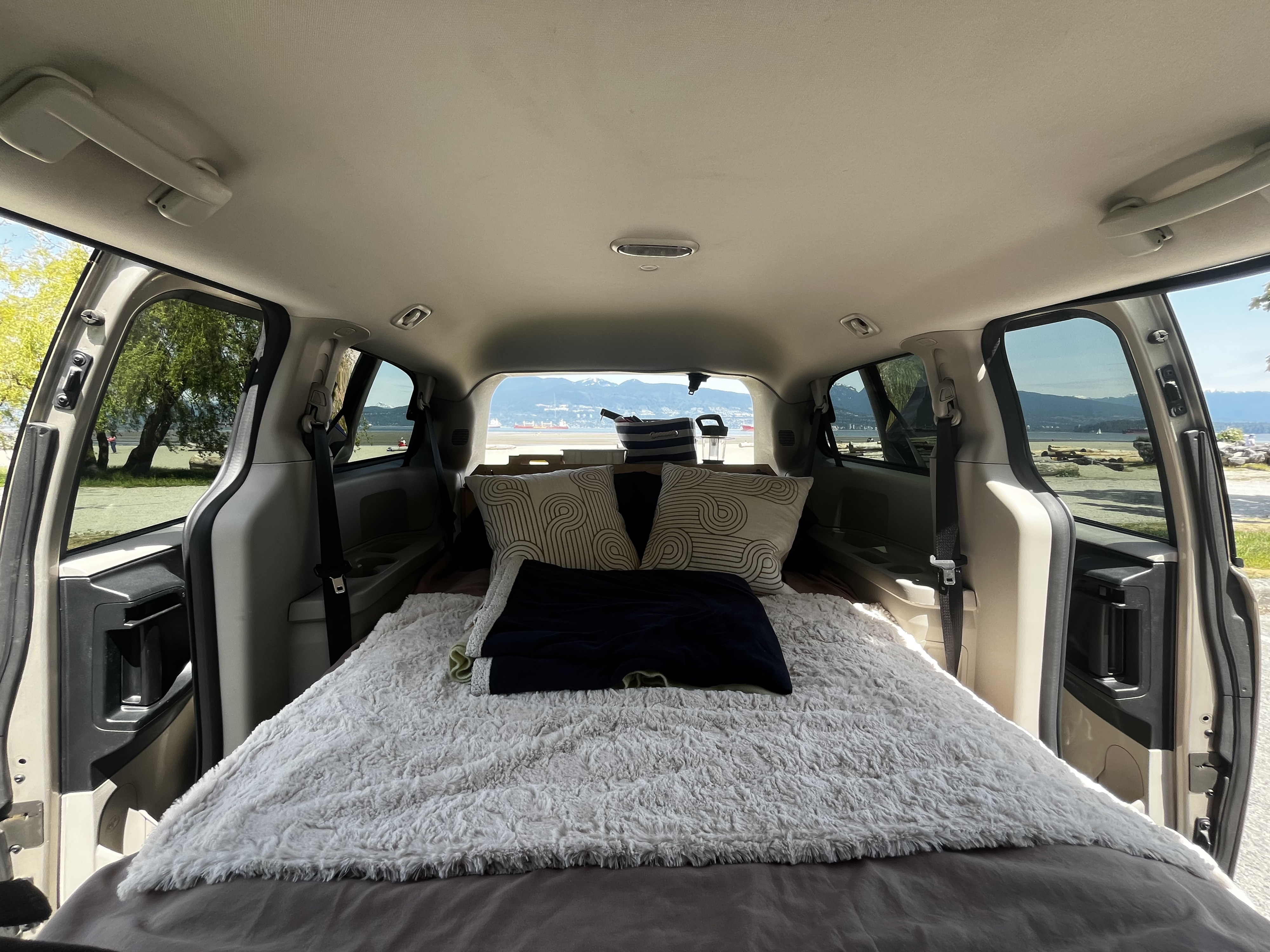 Cozy van bed setup inside an RV rental, offering stunning views of mountains and ocean for your next adventure.. Dodge Grand Caravan 2014