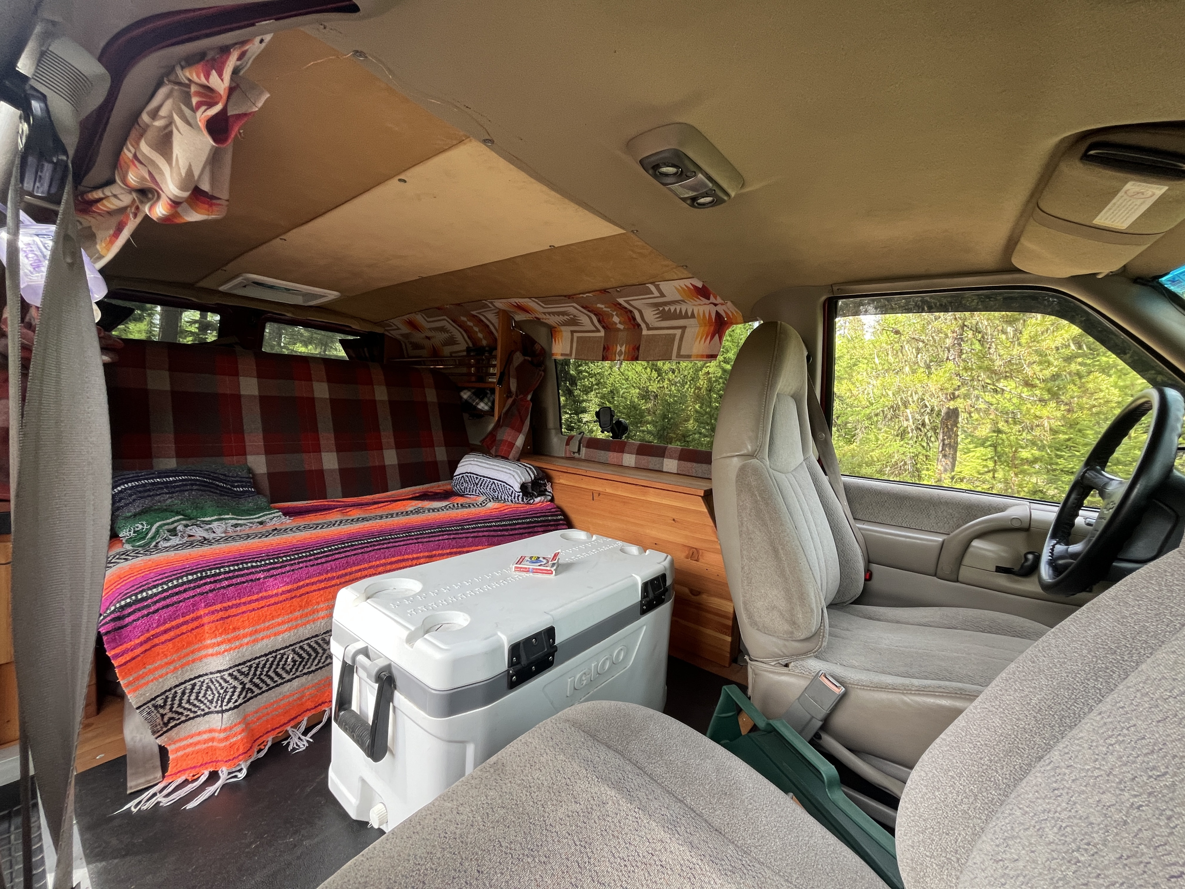 Cozy RV rental interior: Custom camper van features a built-in bed with colorful blankets, a cooler, and wooden storage.. Chevrolet Astro Van 1997