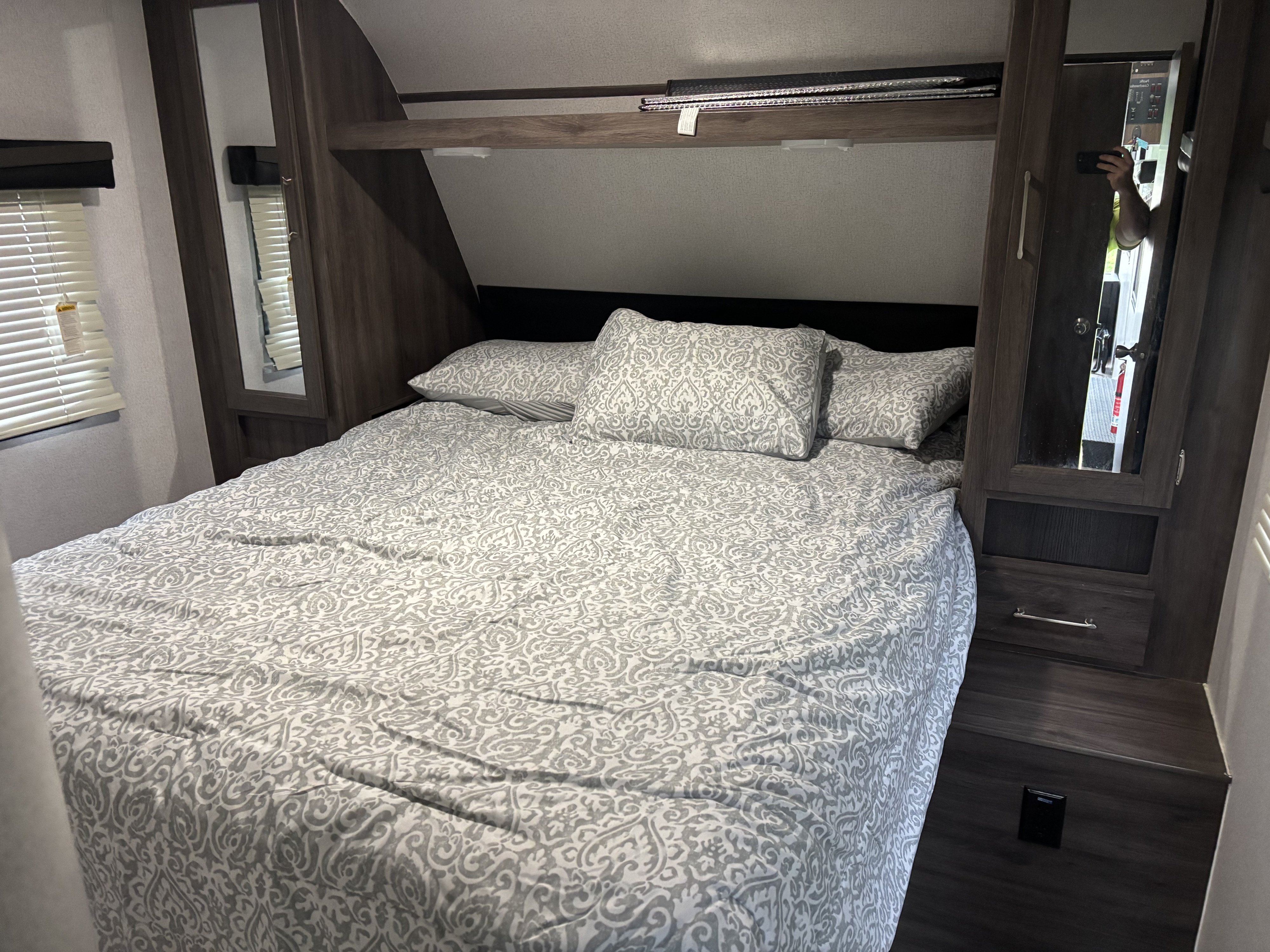 Relax in this RV rental bedroom. Features a comfortable bed with patterned bedding, overhead storage, and side cabinets.. Pacific Coachworks Powerlite 2021