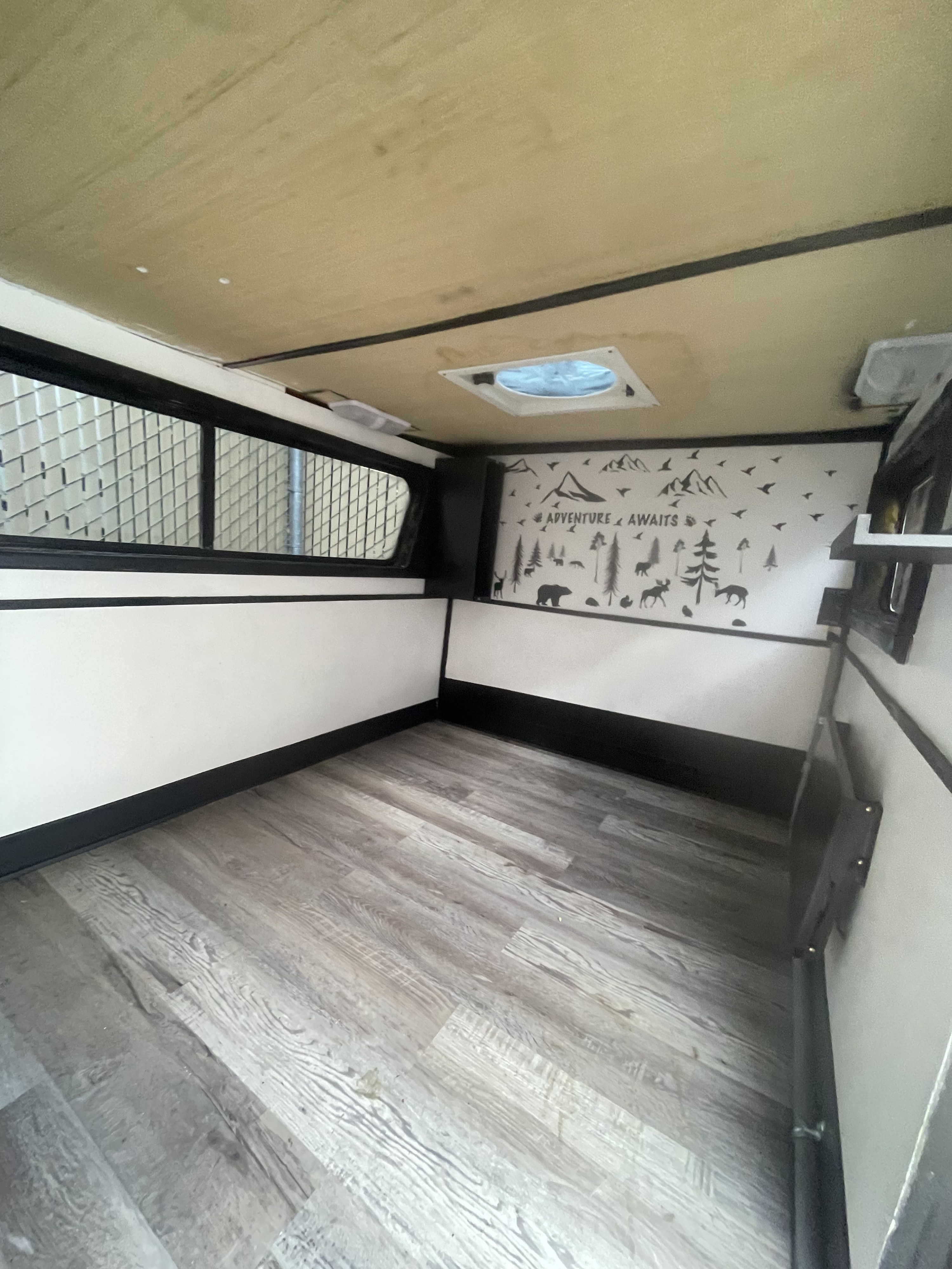 Spacious rv rental interior: wood-look floor, white walls with black trim, and an "ADVENTURE AWAITS" mural.. Mini Teardrop 2021