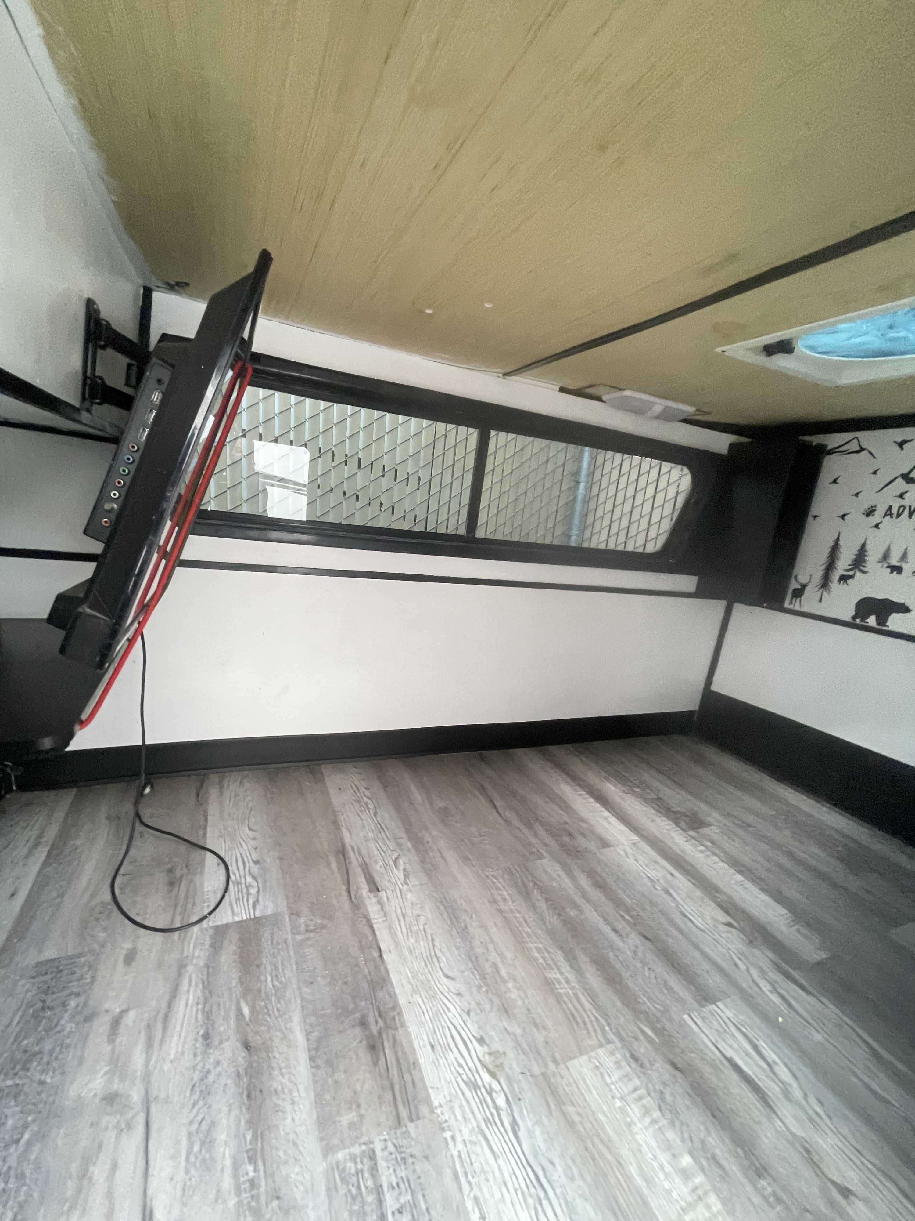 Interior of an RV rental showing a mounted TV, gridded window, wood floor, and adventure wall decals.. Mini Teardrop 2021