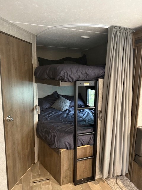 RV rental interior with cozy bunk beds, dark bedding, and a privacy curtain. Ideal sleeping area for families.. Dutchmen Coleman Lantern 2020