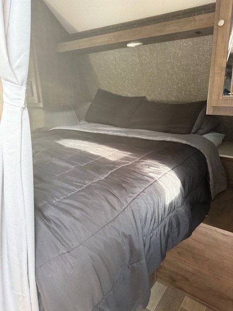 Cozy RV rental bedroom with a large bed, overhead storage, and patterned walls. Perfect for travel.. Dutchmen Coleman Lantern 2020