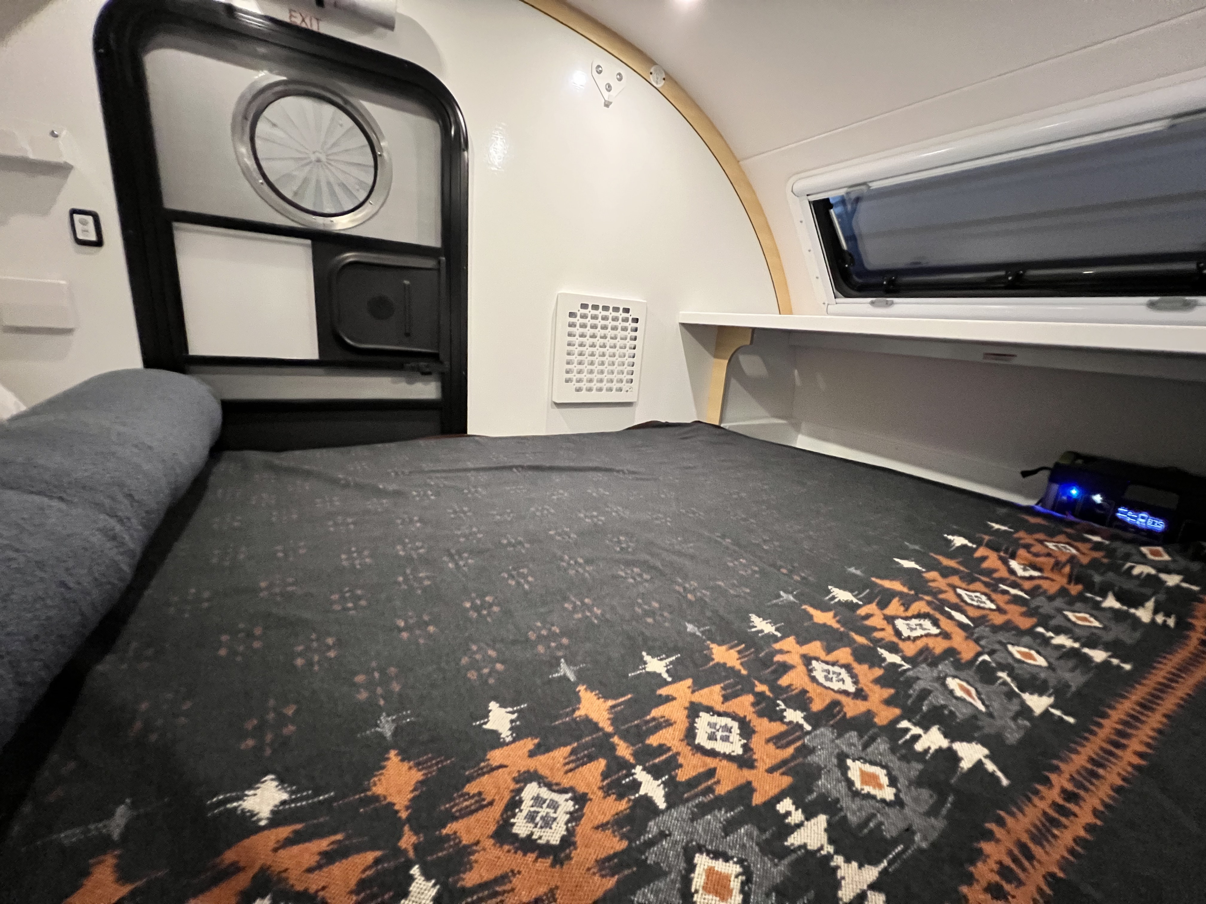Cozy RV rental interior: a comfortable bed, entrance door, wall vent, and side window for compact travel.. Bean Trailer Bean Stock 2.0 2024