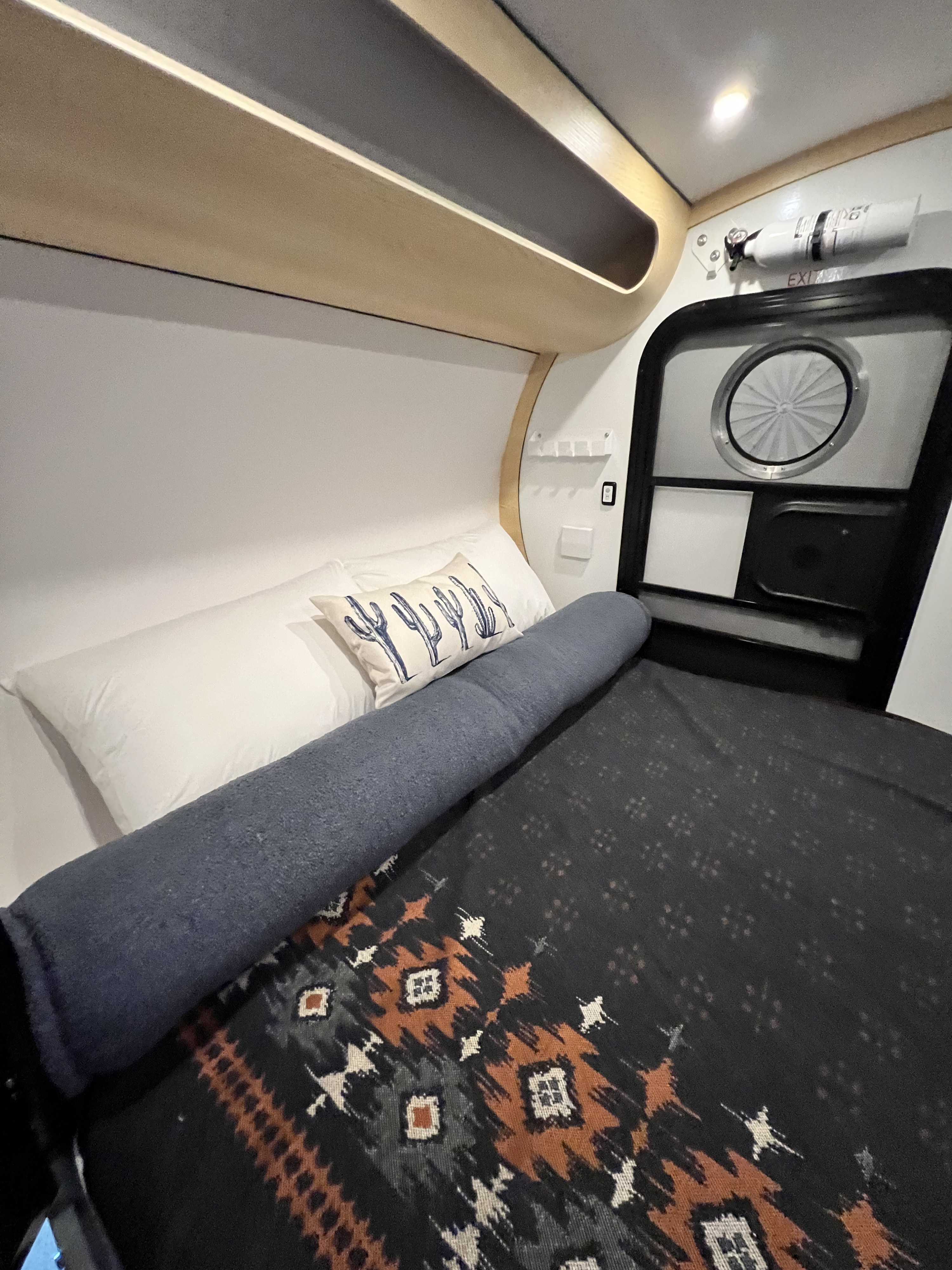 Step inside this cozy RV rental's sleeping area, featuring a Southwestern blanket, cactus pillow, and compact design.. Bean Trailer Bean Stock 2.0 2024
