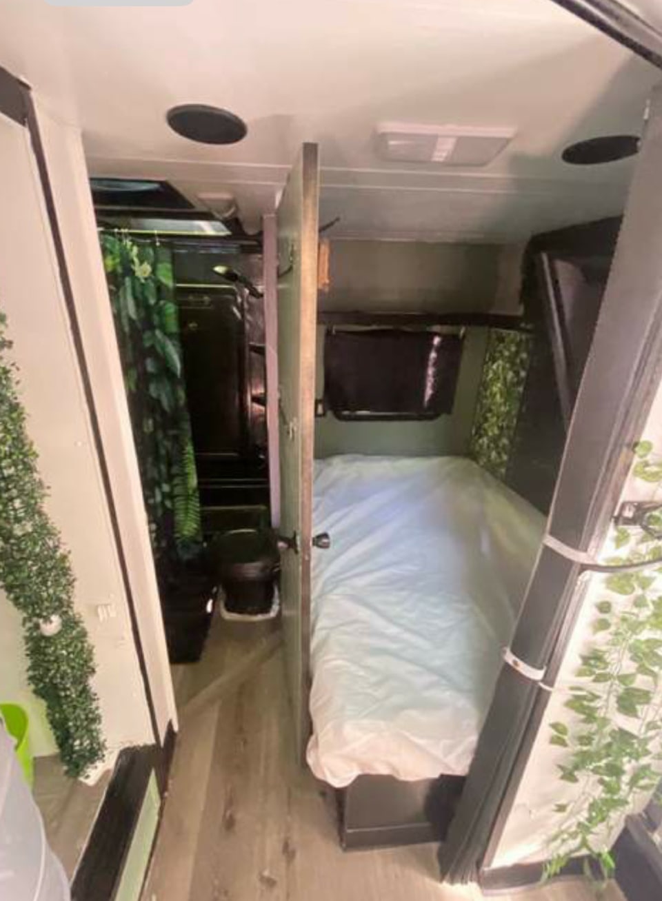 Inside an RV rental: Compact living area with a white-sheeted bed and a small bathroom featuring a green shower curtain.. Fleetwood Prowler 1996