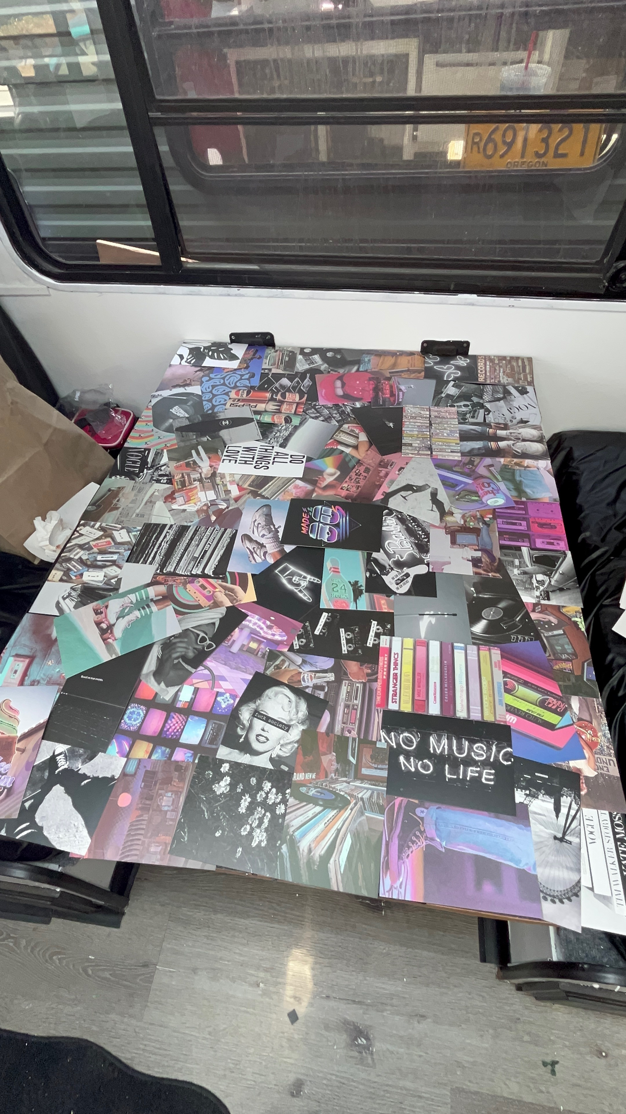 Vibrant music/pop culture collage on an RV rental table. Personalized decor inside a vehicle, with window reflections visible.. Skyline Century 1985