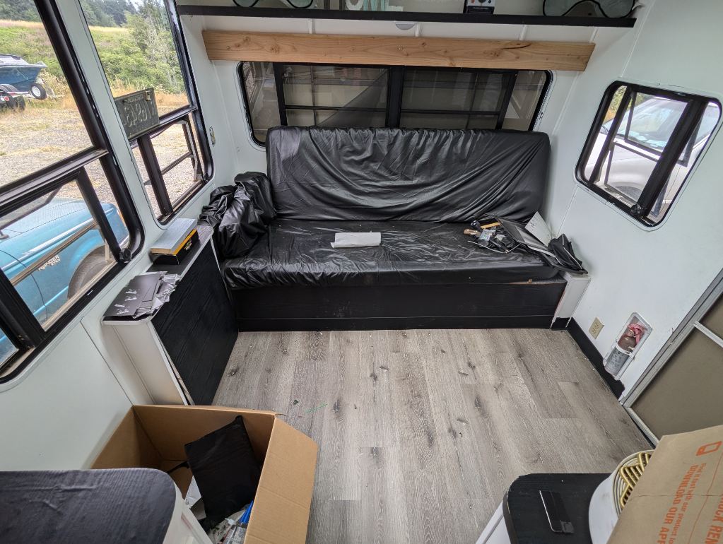 RV rental interior: A white-walled cabin space featuring a long black upholstered bench, light wood floor, and large windows overlooking the outside.. Skyline Century 1985