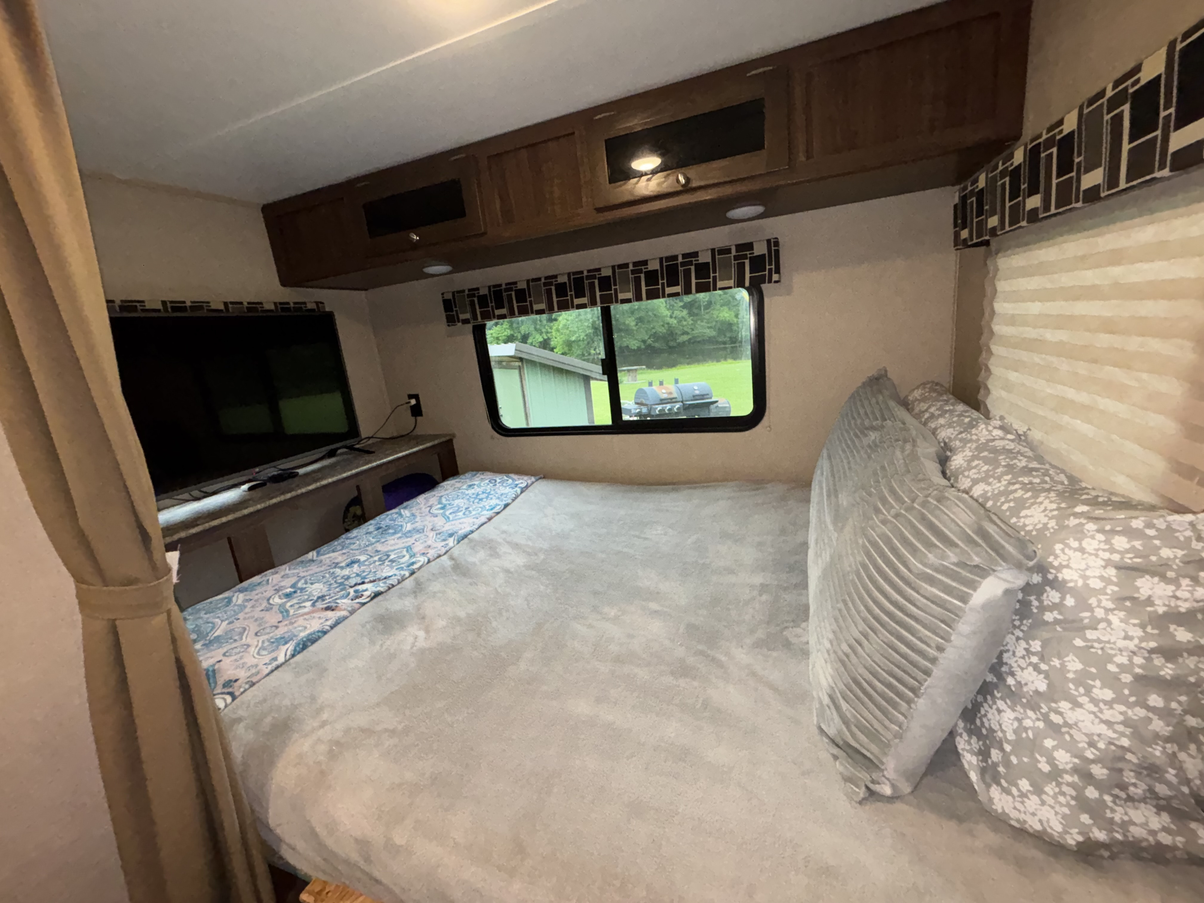 Cozy RV rental bedroom with comfortable bed, TV, overhead storage, and a scenic window view.. Dutchmen Coleman Light LX 2018