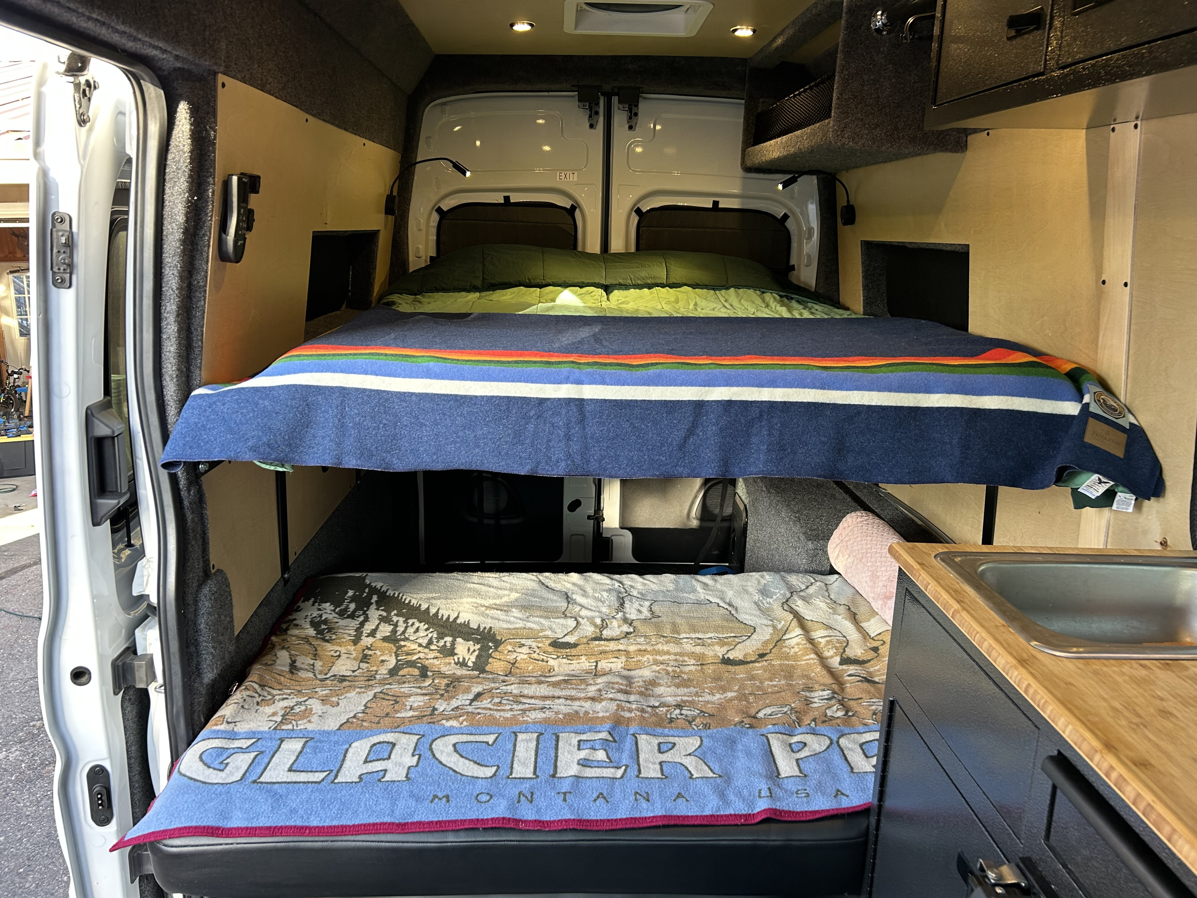 RV rental: Cozy camper van interior with stacked beds, a Glacier Park blanket, and a compact sink.. Ford Transit 2023