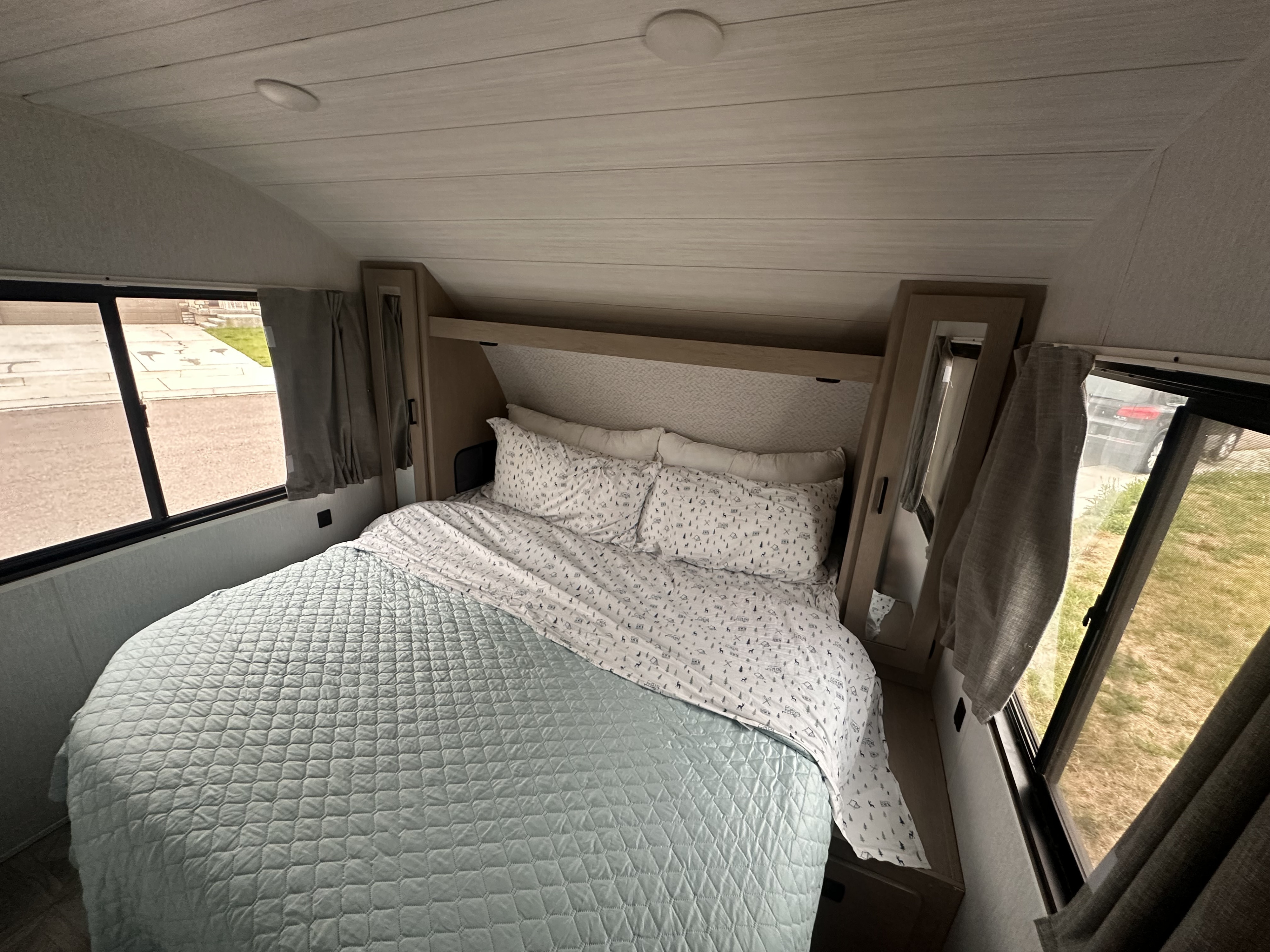 Cozy RV rental bedroom: Features a light blue quilted bed, nature-patterned sheets, and windows with curtains for comfortable travel.. Forest River Wildwood X-Lite Platinum 2024