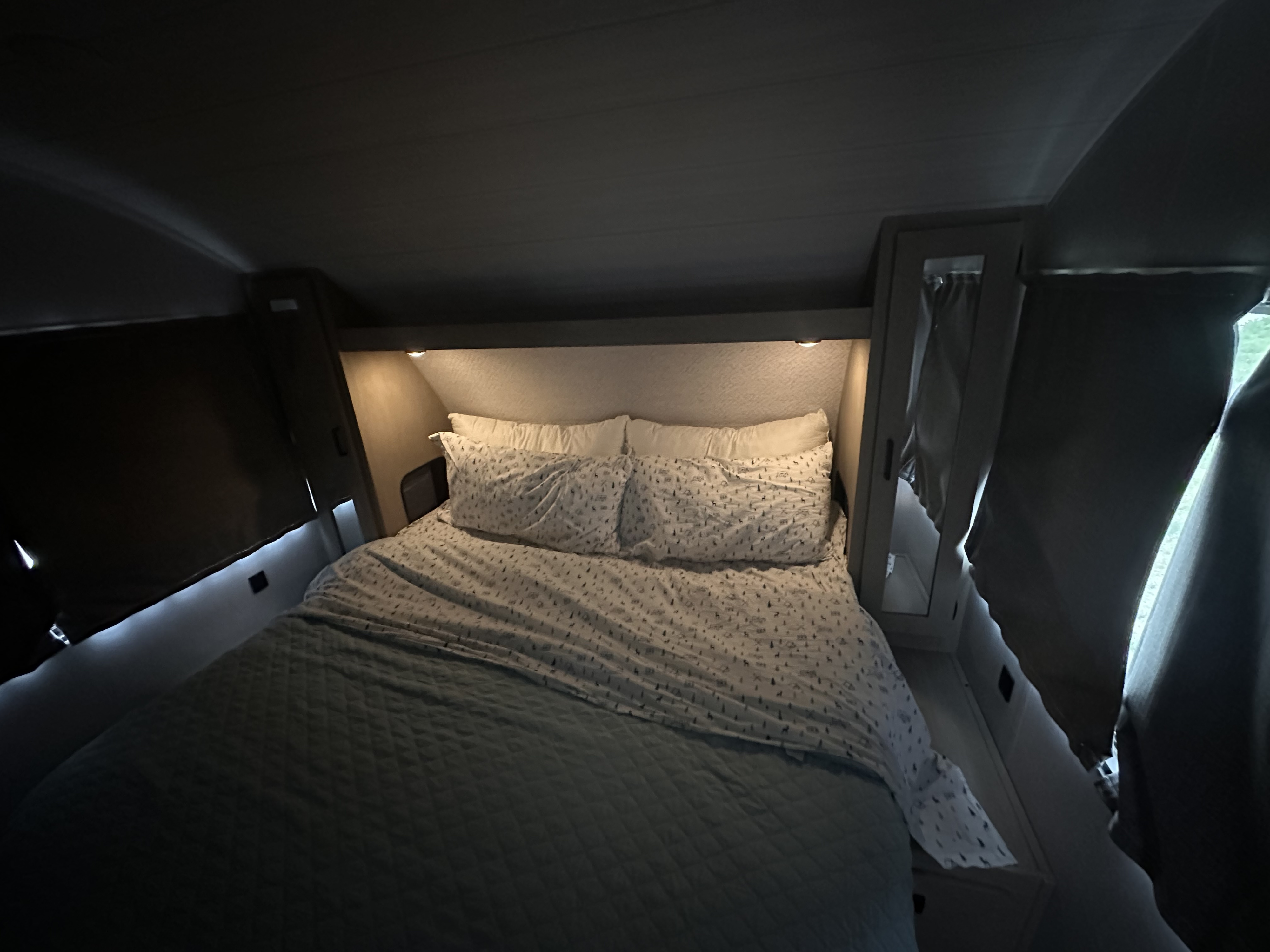 Comfortable RV rental bedroom featuring patterned bedding, soft pillows, and warm ambient lighting above the bed.. Forest River Wildwood X-Lite Platinum 2024
