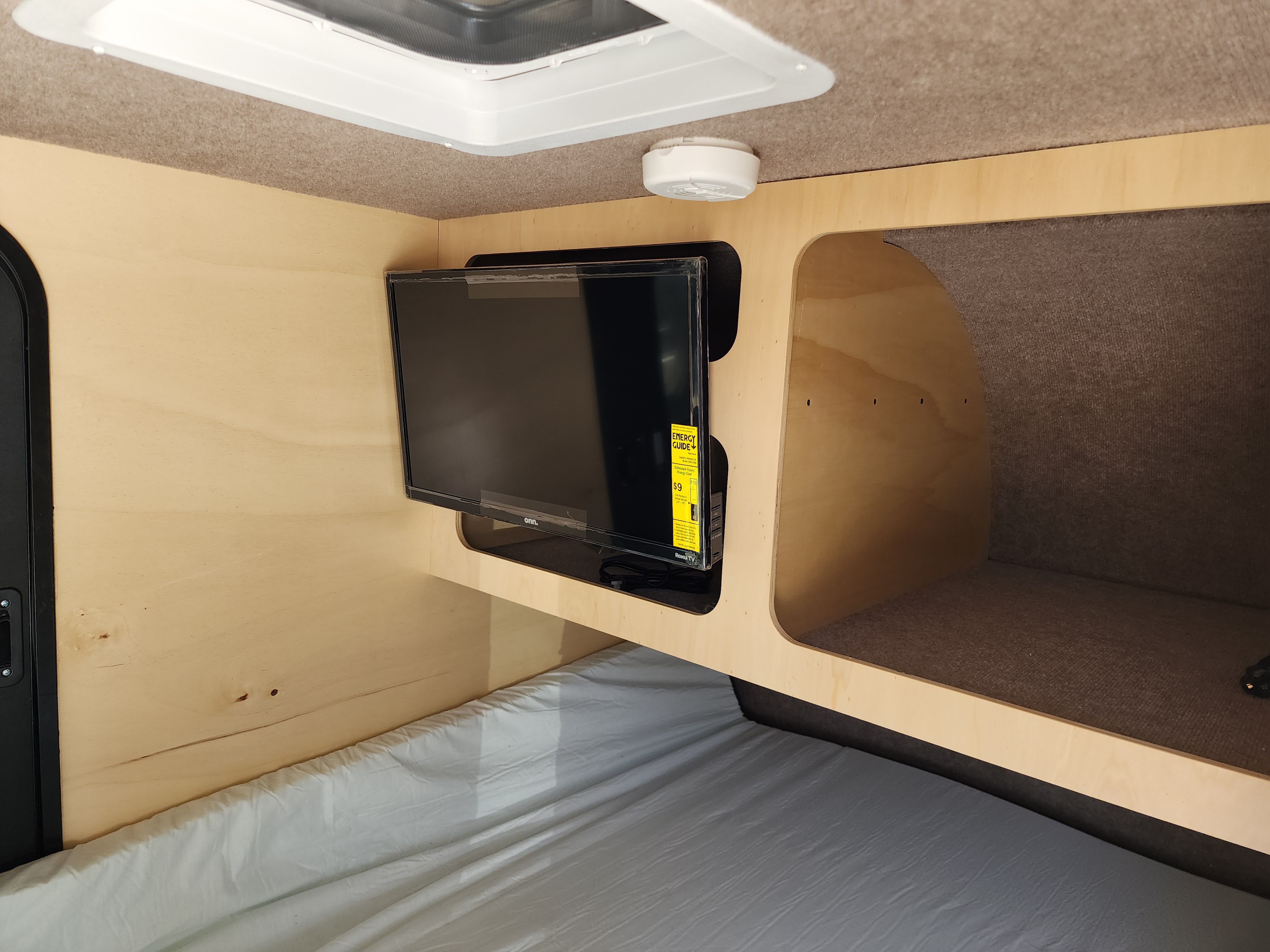 RV rental interior showing a comfortable bed, wall-mounted TV, and storage cubby. Perfect for road trips!. Off Grid Trailers Off Grid Trailers Trailer 2021