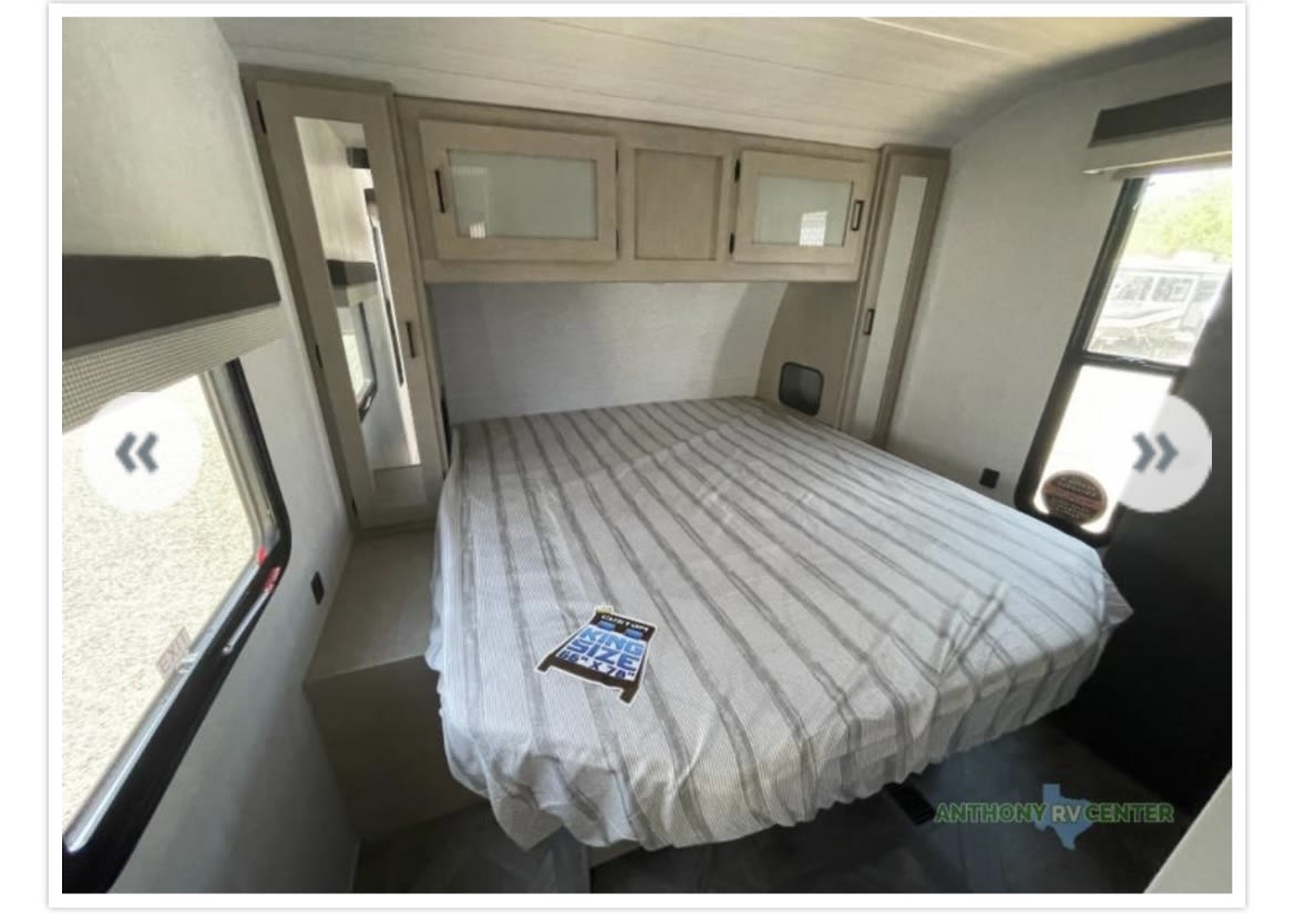 RV rental bedroom with a striped king-size bed, ample overhead cabinets, and bright windows, creating a cozy RV interior.. Forest River Wildwood 2023