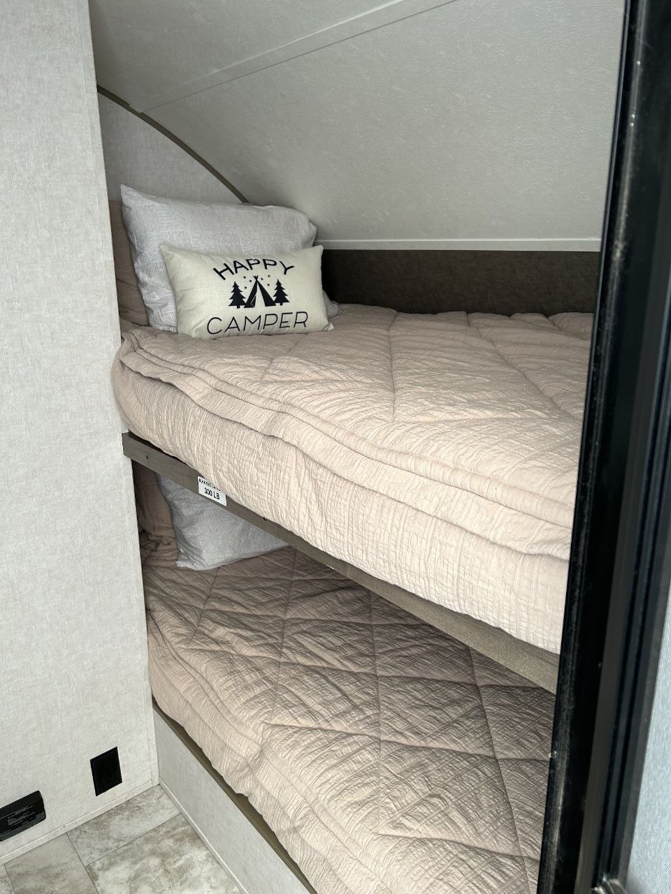 RV rental interior featuring cozy bunk beds with pink bedding and a "Happy Camper" pillow, ready for guests.. Forest River R-Pod 172 2019