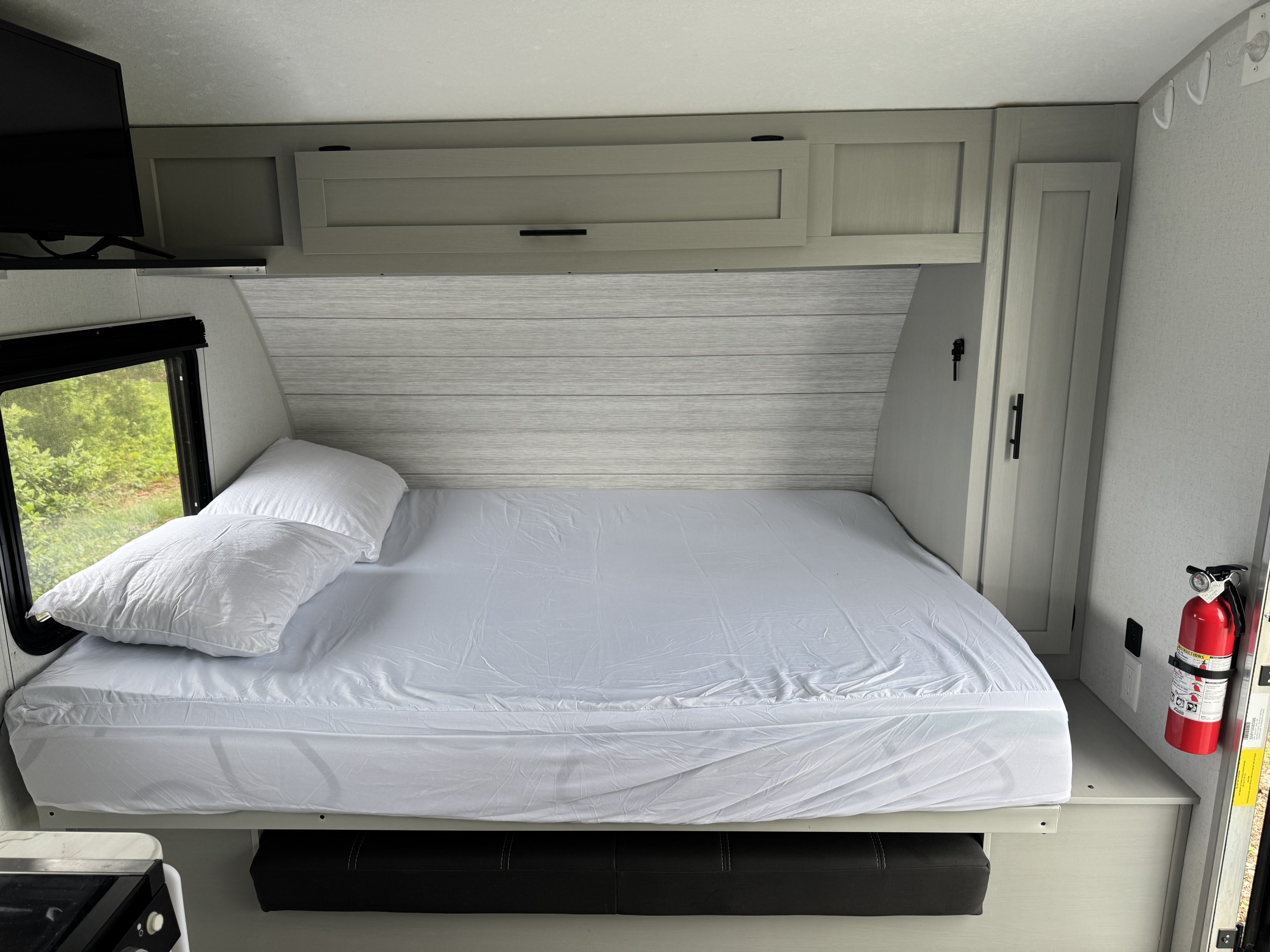 Cozy RV rental bedroom featuring a bed with white linens, overhead cabinets, a TV, and a view of nature.. Forest River Salem FSX PLATINUM 2021