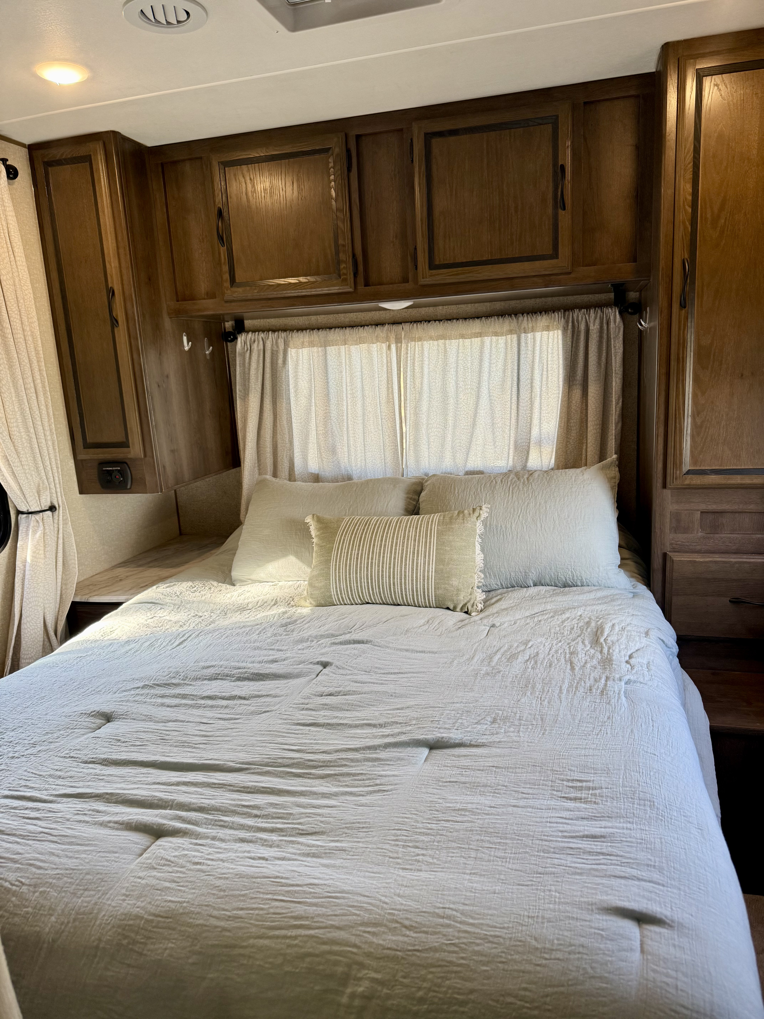 Interior of a cozy RV bedroom with light bedding, wooden cabinetry, and curtains – ideal for an RV rental.. Forest River Coachmen Freelander 2018