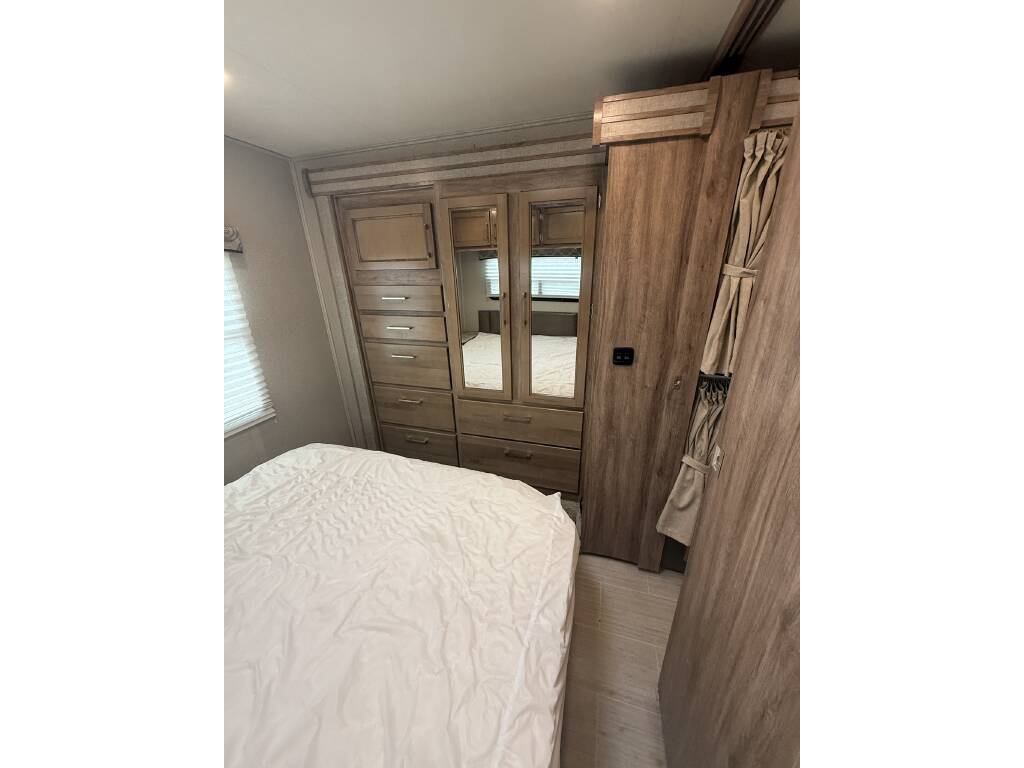 RV rental bedroom interior features a bed, built-in wooden wardrobe with a mirrored dresser, optimizing space.. Entegra Coach Odyssey 2020