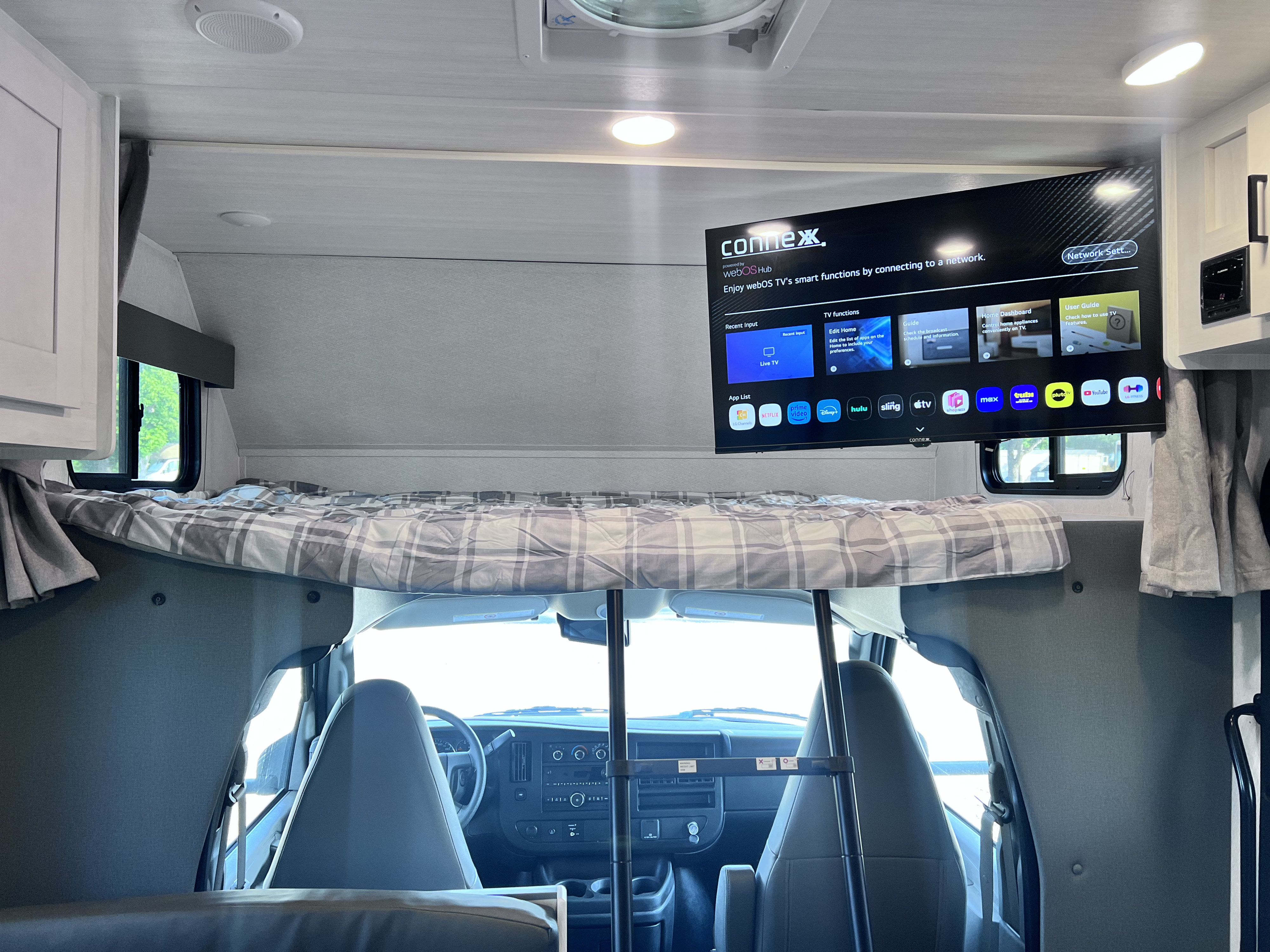 RV rental interior: elevated bunk bed over cab, with a large smart TV showing streaming apps for entertainment.. East to West Entrada 210NSC 2025