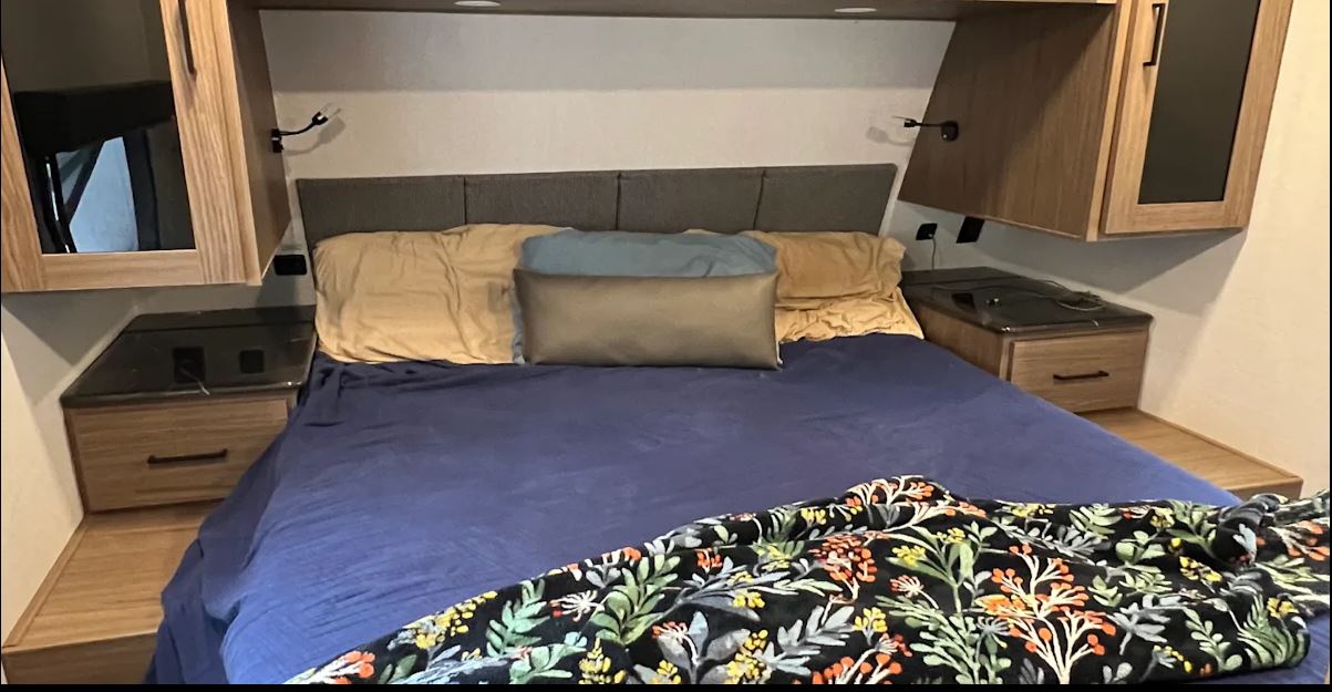 Comfortable RV rental bedroom with a large bed, built-in nightstands, overhead storage, and reading lights.. Alliance Delta 251BH 2024