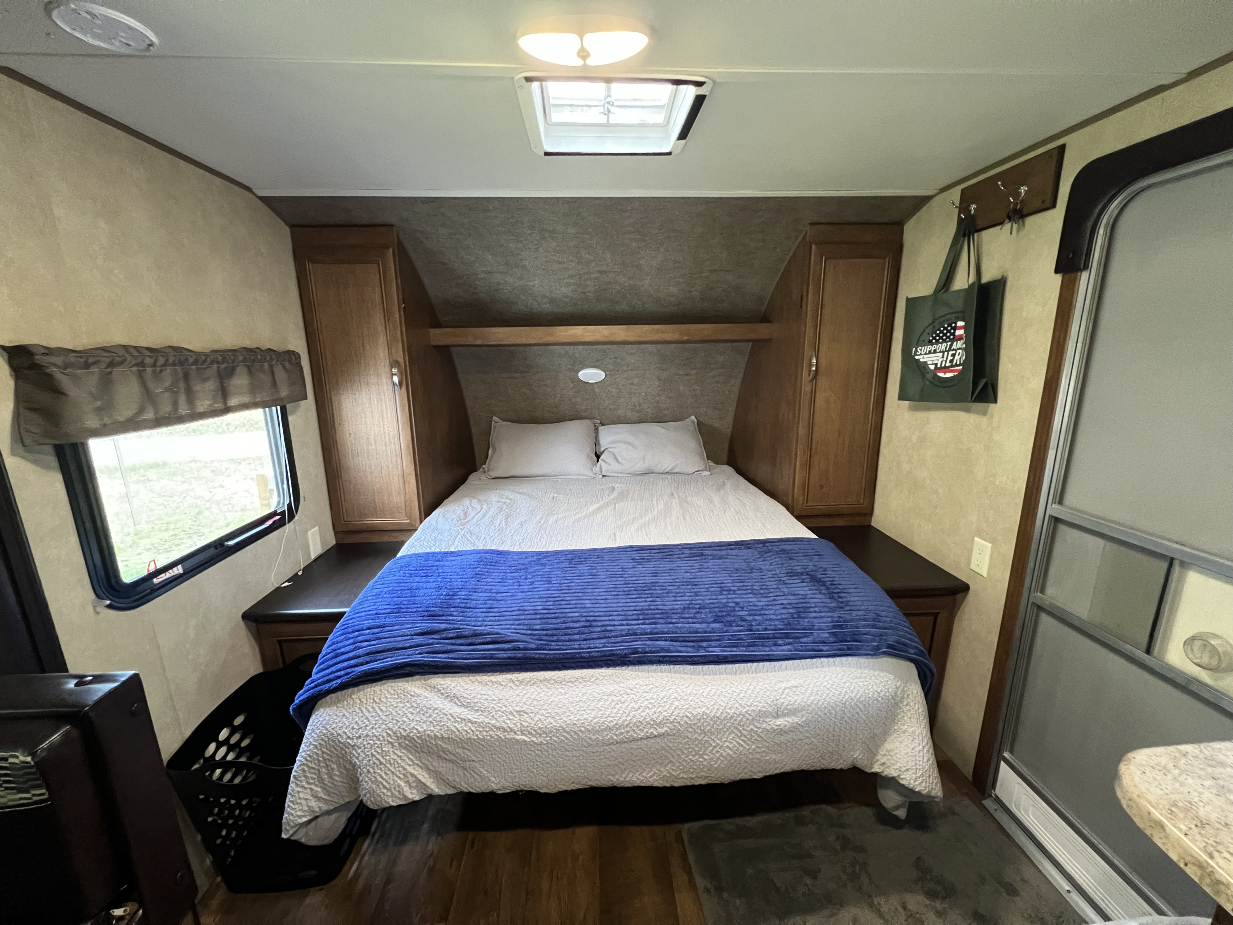 Cozy RV rental bedroom featuring a comfortable queen bed, window, storage, and compact living space.. Forest River Wildwood X-Lite 2017