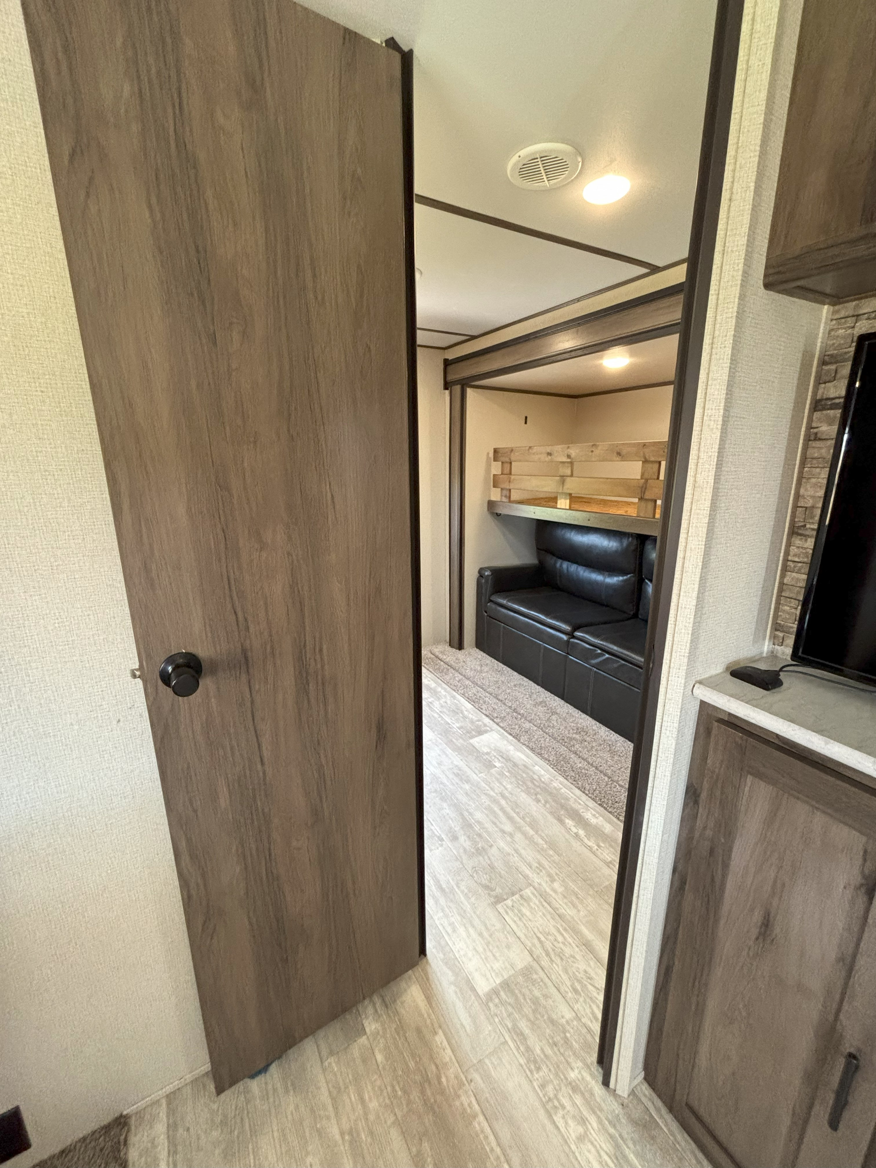 RV rental interior: A door opens to a bunkhouse with a black sofa and wooden bunk beds.. Prime Time Avenger 32QBI 2020