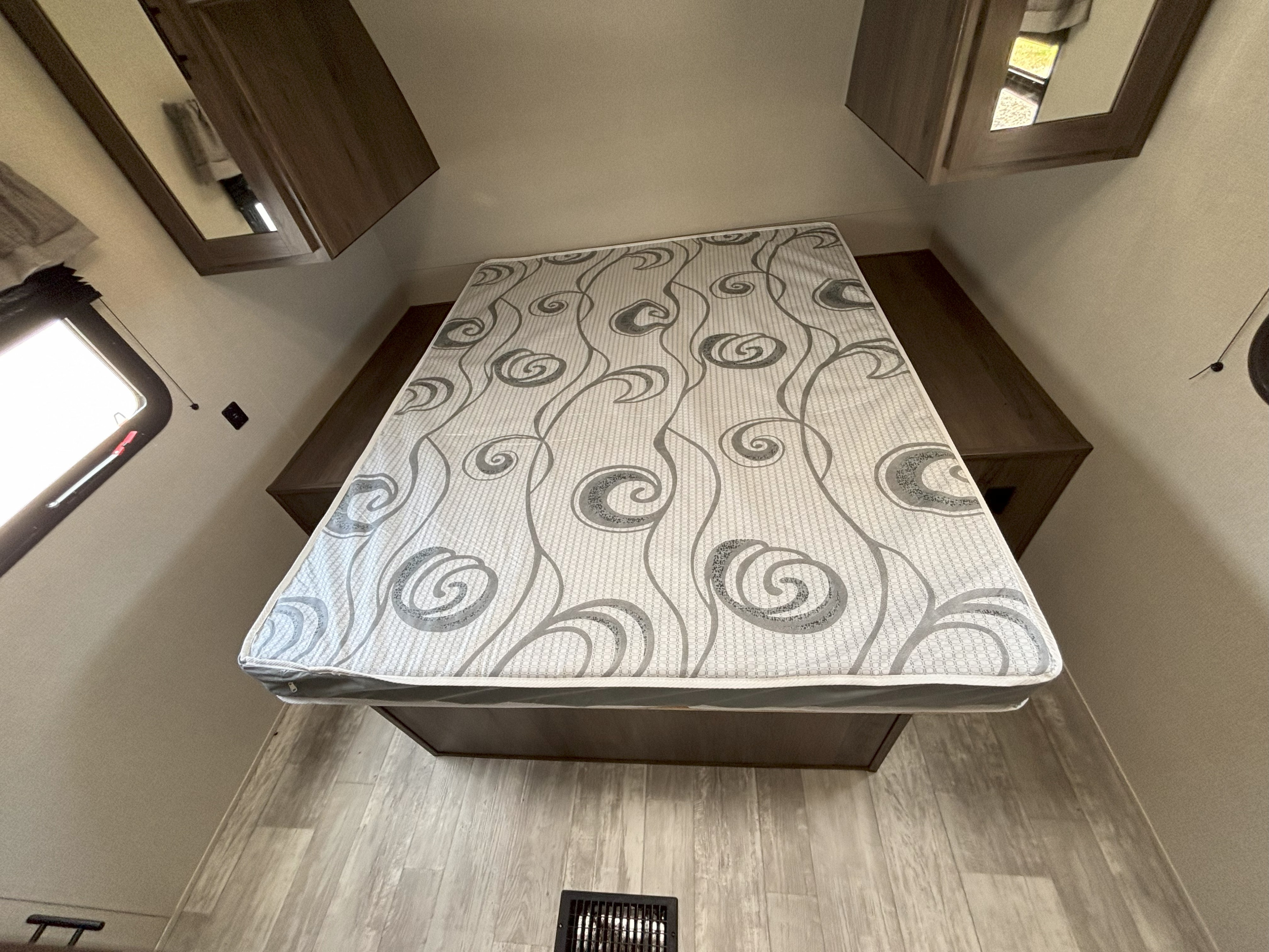 Inside an RV rental: a cozy bedroom with a patterned mattress, wooden base, and mirrored overhead storage.. Prime Time Avenger 32QBI 2020