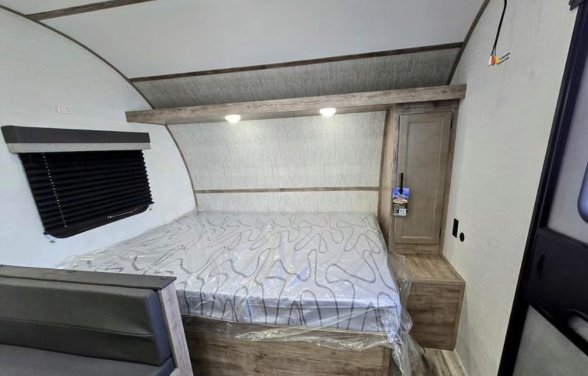 Discover this cozy RV rental bedroom. Features include a new mattress, window with blinds, and built-in storage.. Gulf Stream Kingsport Lite 199DD 2025