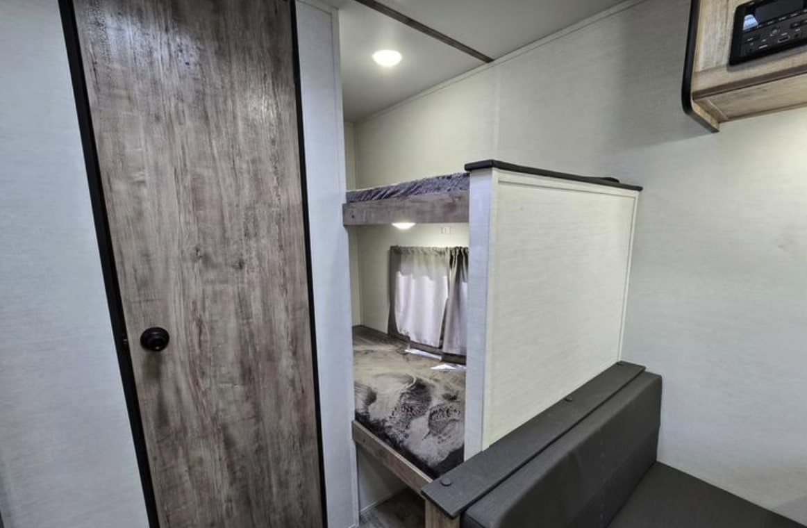 RV rental interior shows a cozy bunk bed area with curtains, a wooden door, and seating.. Gulf Stream Kingsport Lite 199DD 2025