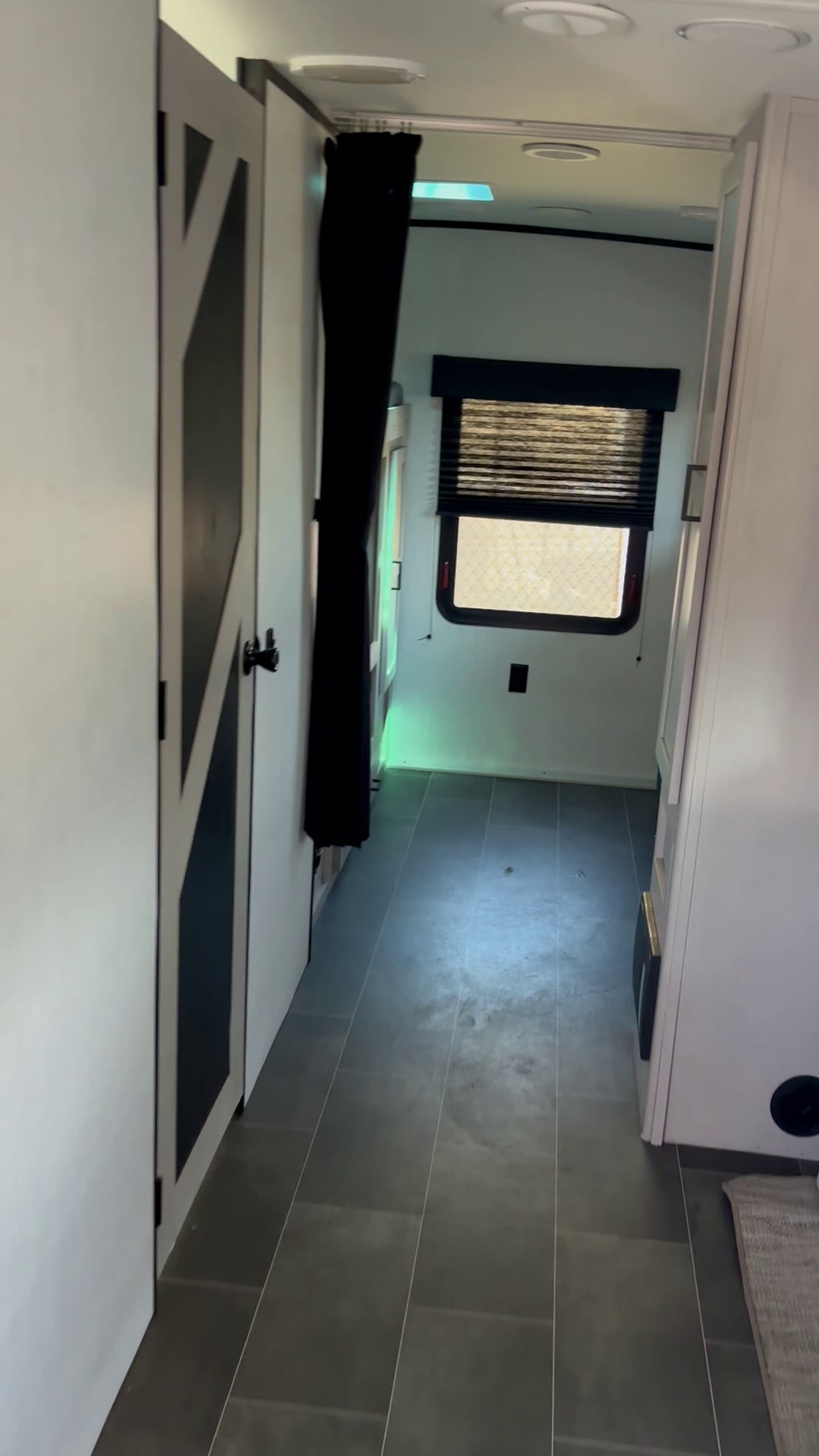 RV rental interior: A modern hallway with gray floor tiles, white walls, and a dark barn-style sliding door. Features a window.. Heartland RVs Mallard 2022