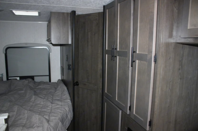 Modern RV rental interior: bedroom with gray bedding, window, and ample wood-toned storage cabinets.. Coachmen Cross Trail 2023