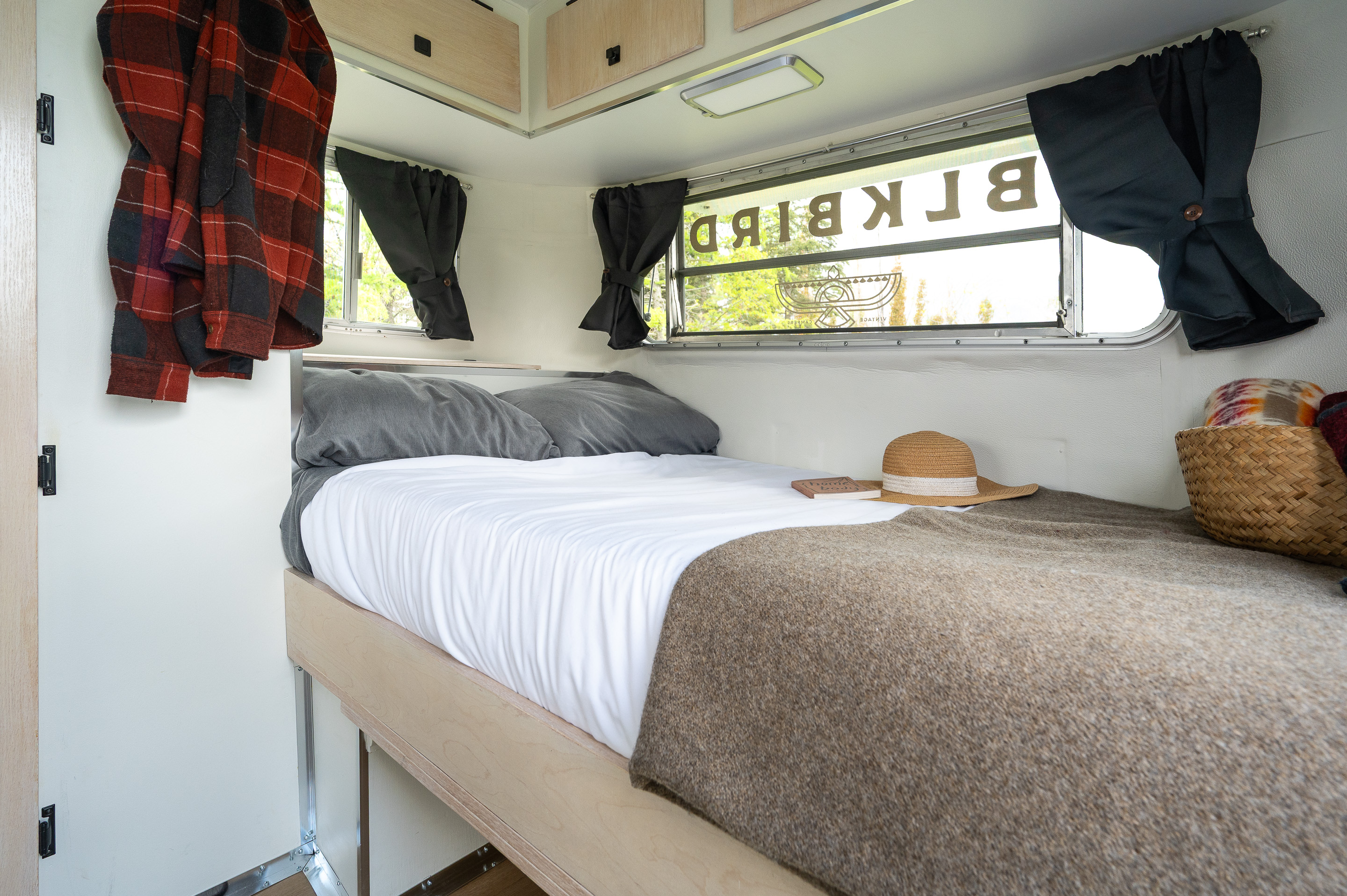 Blackbird Vintage Camper rv rental bedroom: bed with grey pillows, plaid shirt, and window view.. boler boler 1700 1977